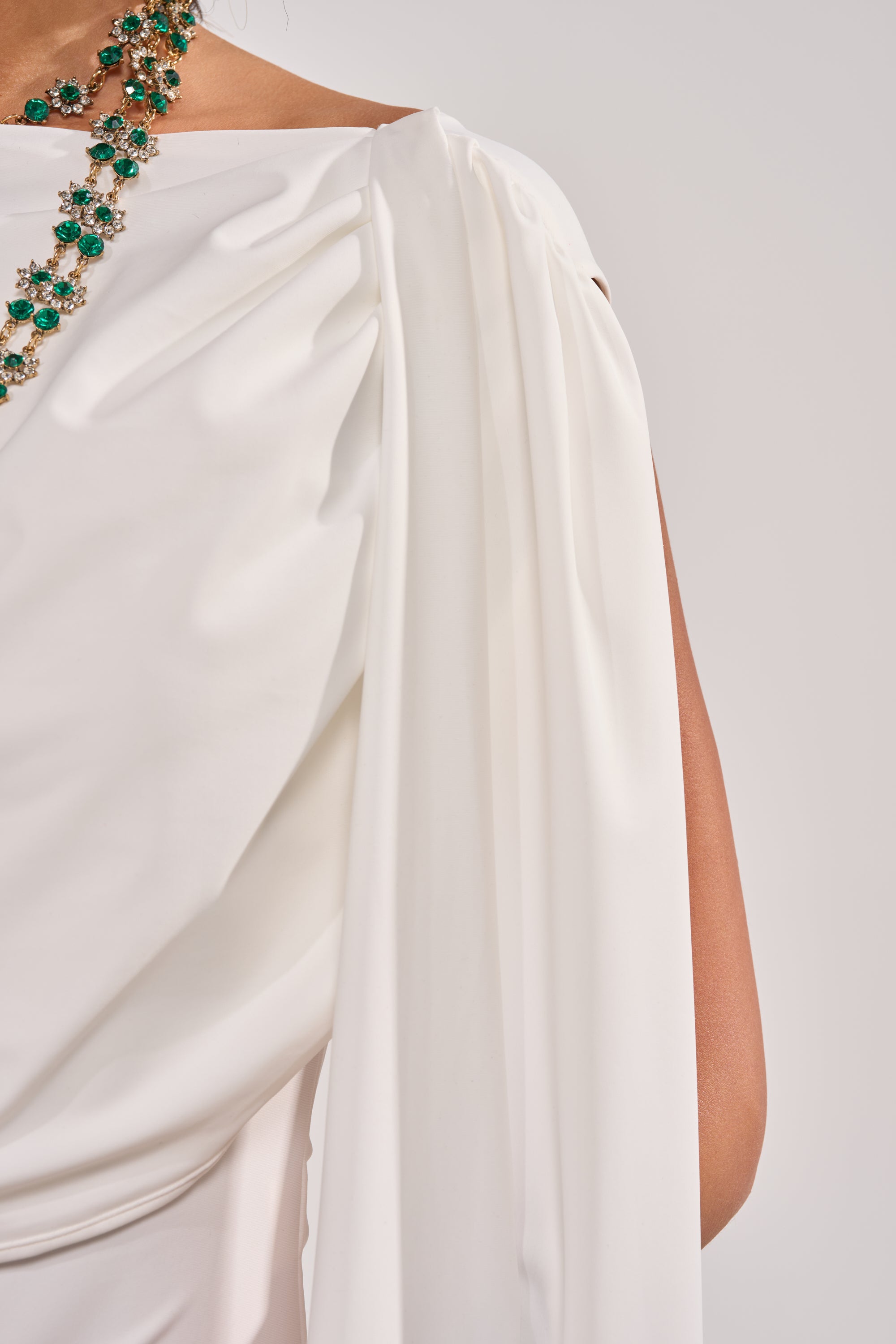 A person wearing the HILLARY SEAMLESS BODYSUIT IN IVORY styled off-shoulder with a green gemstone necklace, shown from the shoulder down against a plain light background. 5