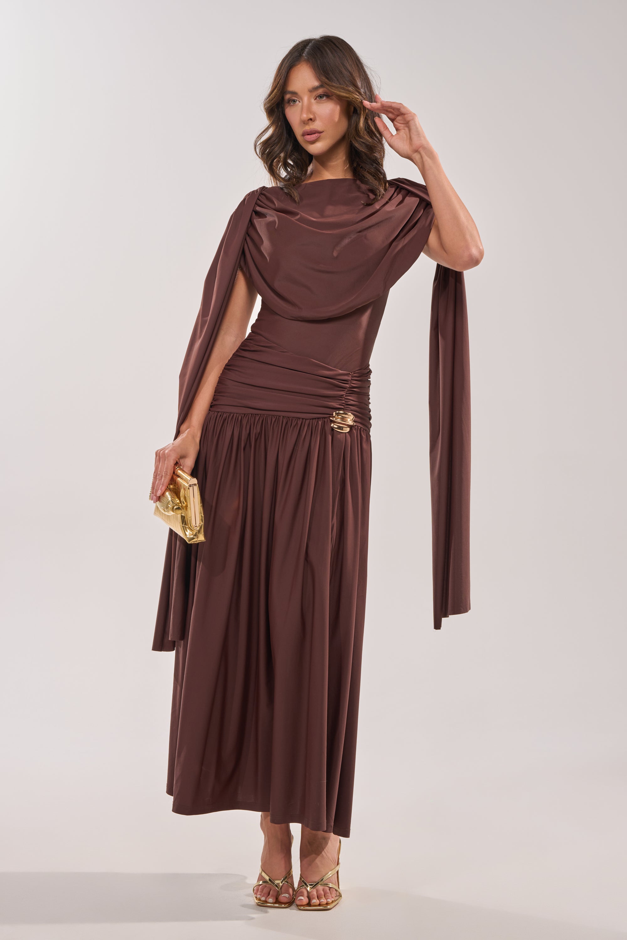 A woman poses in the HILLARY SEAMLESS BODYSUIT, holding a small gold clutch and wearing gold high-heeled sandals against a plain, light-colored background. 2