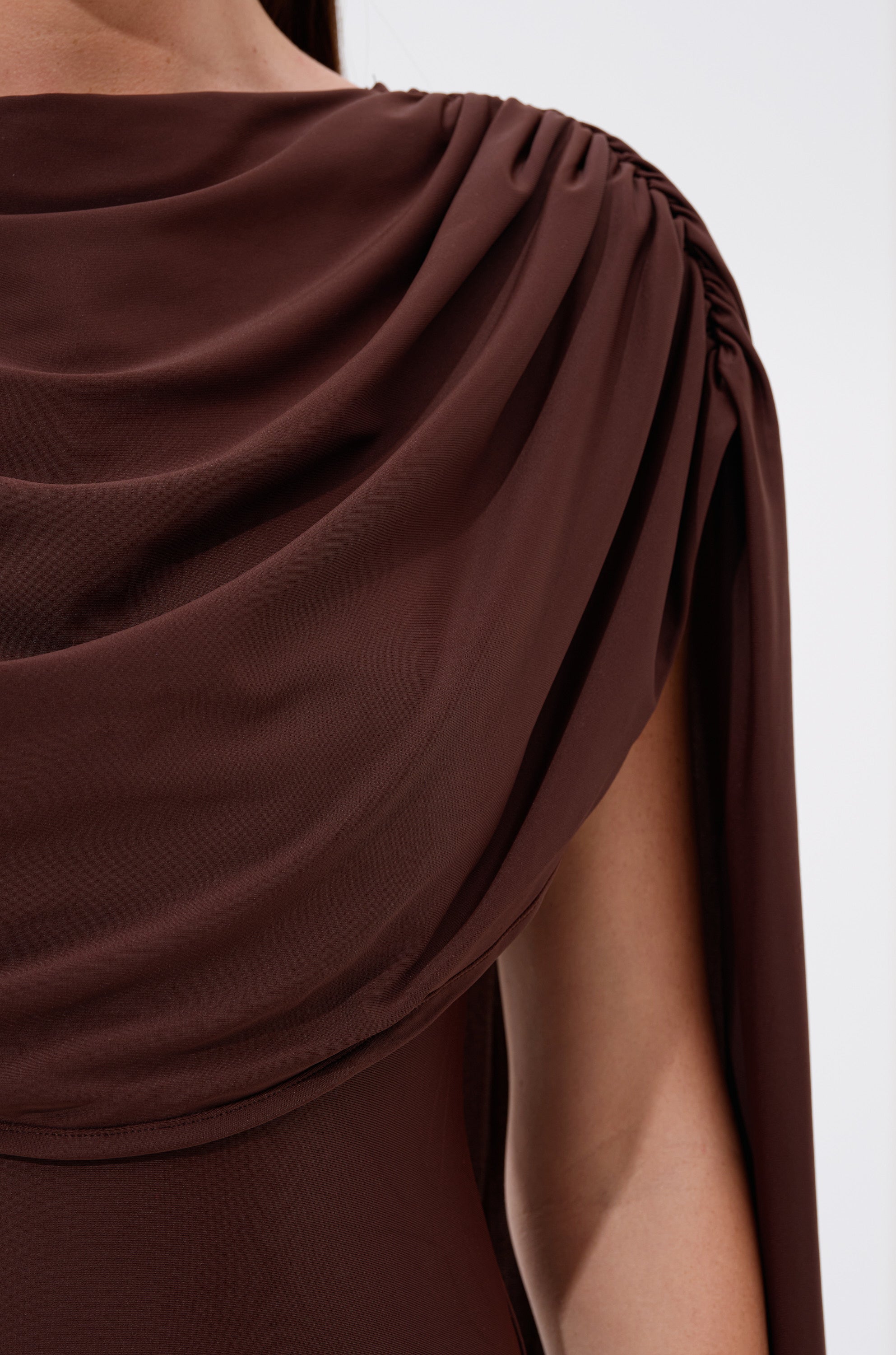 Close-up of the HILLARY SEAMLESS BODYSUIT in chocolate brown, featuring draped fabric with gathered ruching at the shoulder, revealing part of an arm and smooth, flowing material.