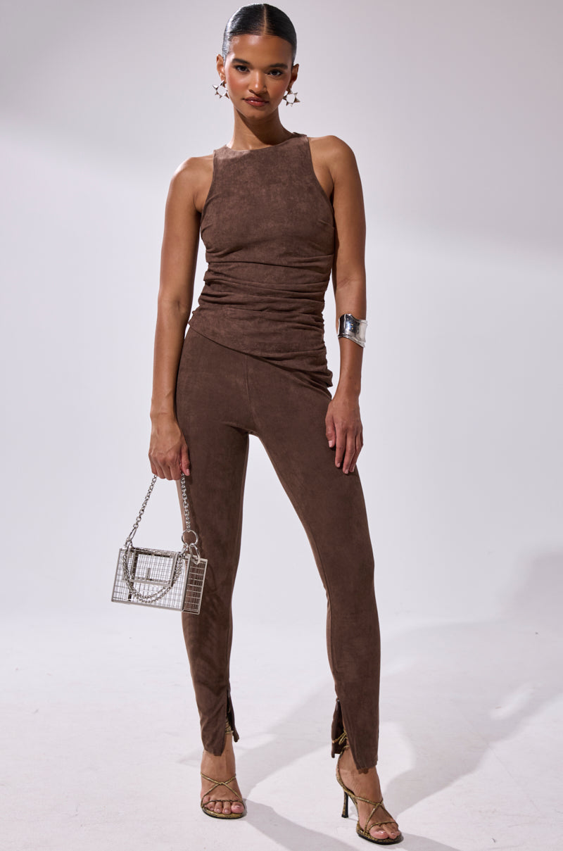 A woman stands confidently in the CHOCOLATE HEAVEN SUEDE BLOUSE, styled with strappy heels, hoop earrings, a small silver handbag, and a sleek bun.