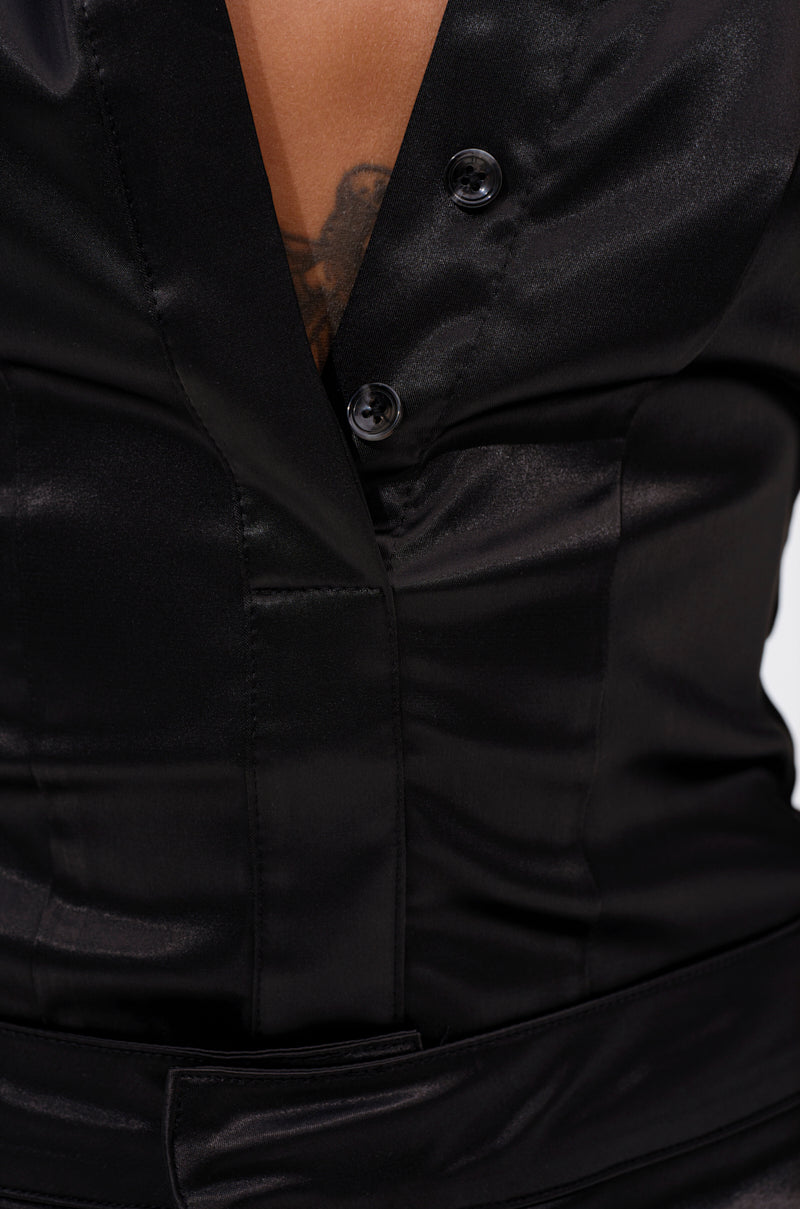 Close-up of a person wearing the DOWN FOR WHATEVER BUTTON DOWN BODYSUIT in black satin, featuring a deep V-neckline and paired with a matching black belt at the waist that reveals part of a chest tattoo. 7
