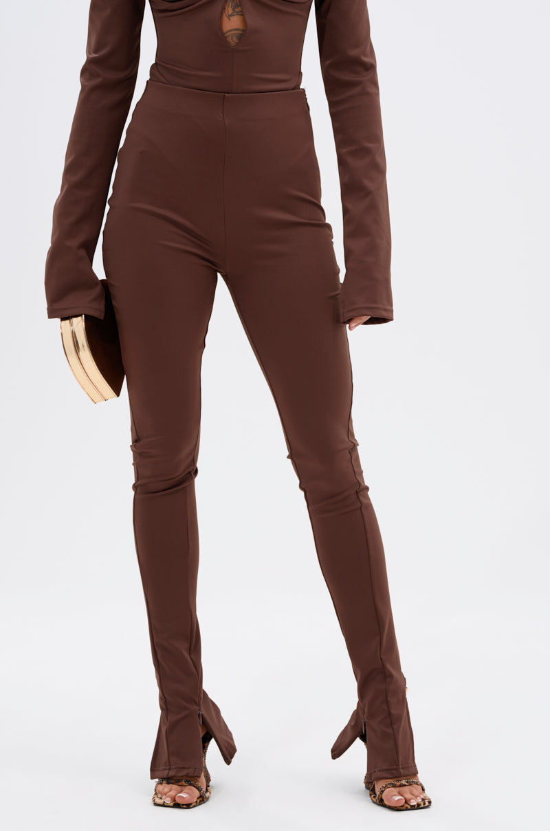 A person wearing the LUX LIFE SEAMLESS LEGGING IN BROWN—high-waisted, sculpting brown leggings with ankle front slits—paired with a matching top, heeled sandals, and a tan clutch, standing against a plain white background. 1