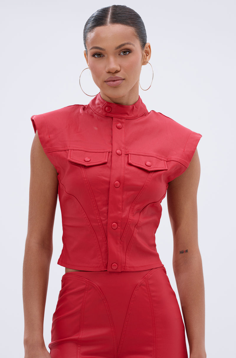 A woman wears the BIG CITY LIVIN FAUX LEATHER BUTTON DOWN, a sleeveless, fitted red faux leather top with front buttons and chest pockets, paired with matching high-waisted pants, hoop earrings, and slicked-back hair.