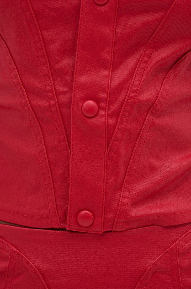 Close-up of the BIG CITY LIVIN FAUX LEATHER BUTTON DOWN in red, showcasing a structured, corset-inspired silhouette with covered buttons and vertical seams. The smooth faux leather is fitted and cropped, paired with matching red bottoms for a modern vibe.