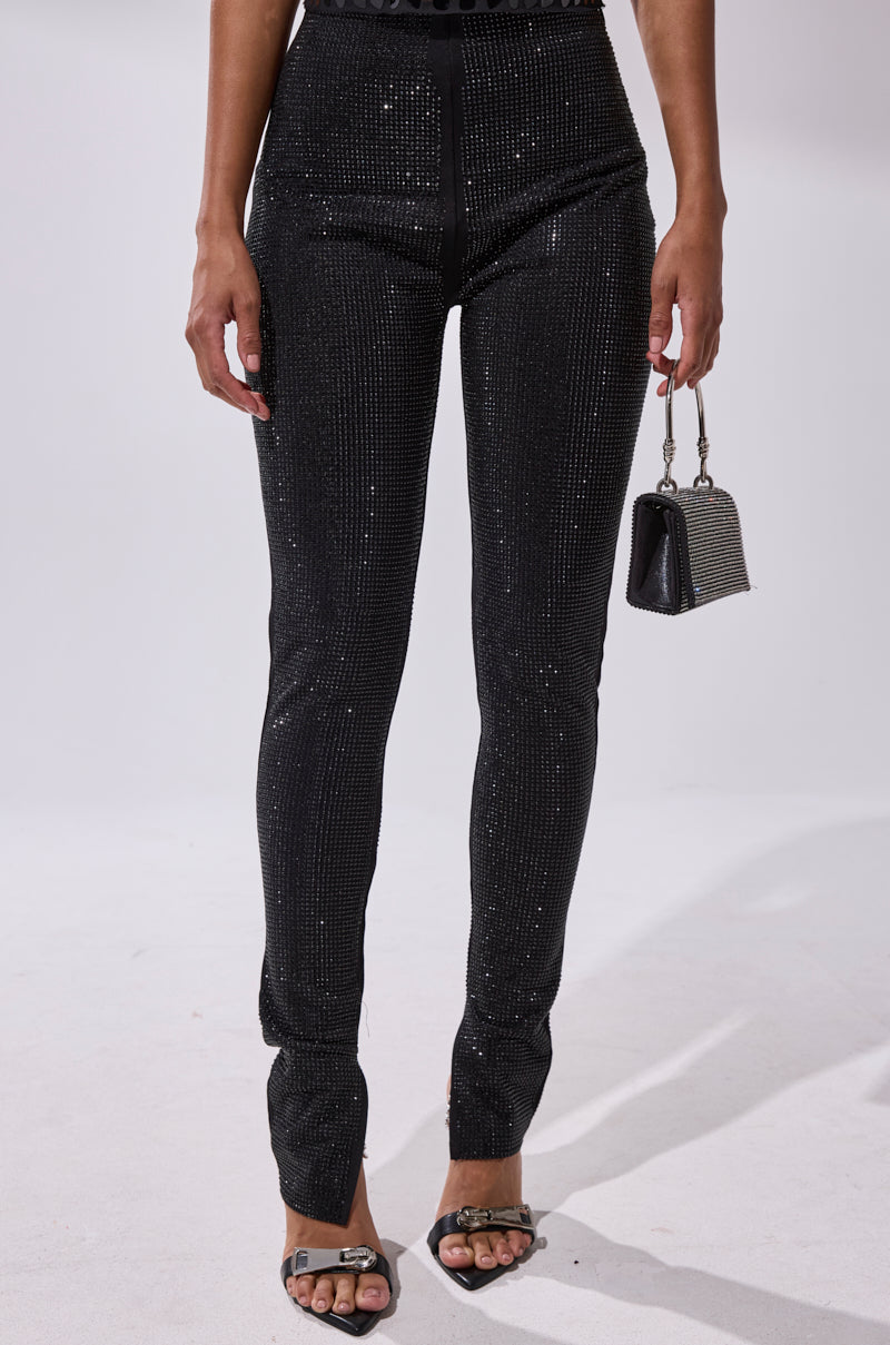 A person is wearing the SPARKLE QUEEN RHINESTONE LEGGING—high-waisted, black, and sparkly—paired with black heeled sandals and holding a small gray handbag with a short handle, against a plain white background.