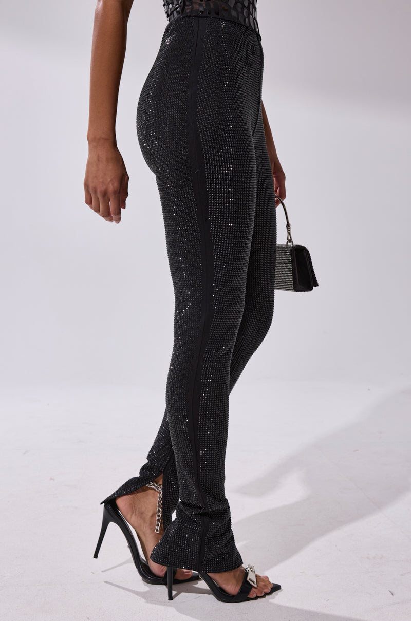 Wearing the SPARKLE QUEEN RHINESTONE LEGGING and black high-heeled sandals, a person stands on a white floor with a small black handbag against a plain, light background.
