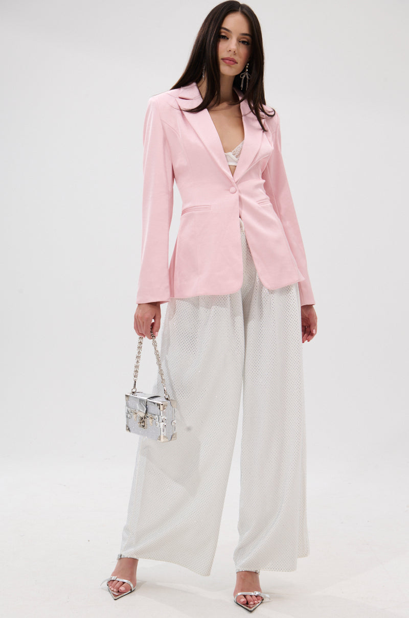A woman stands against a white background wearing the DON'T MAKE ME BLUSH SATIN BLAZER over a white lace top and wide-legged pants, accessorized with a silver handbag, silver heels, and styled straight brown hair. 5
