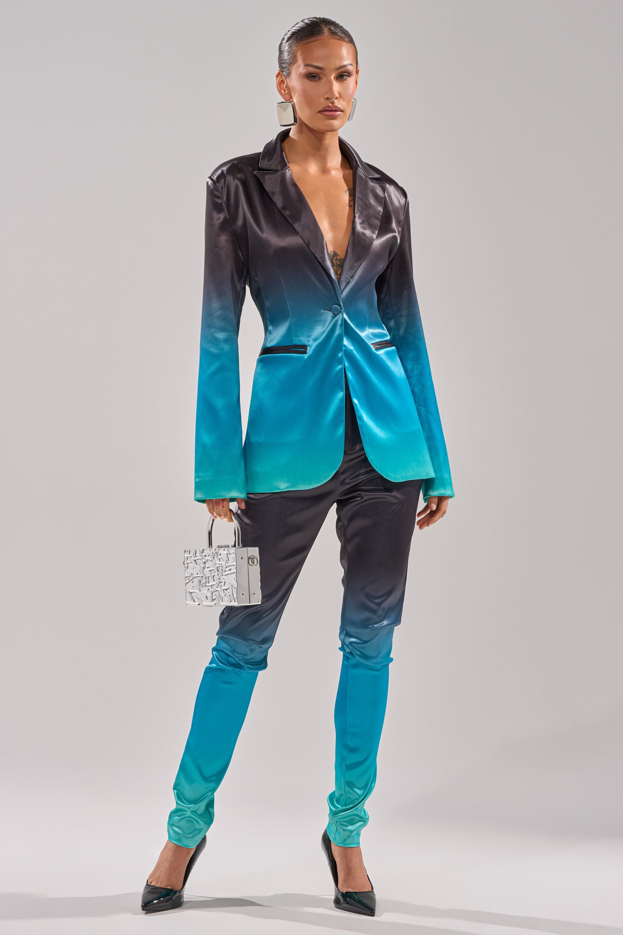 A woman poses confidently in the NIGHT AND DAY OMBRE SKINNY TROUSER, styled with black heels and a white handbag. Her slicked-back hair complements the ombre skinny trousers as she stands against a simple light background. 0