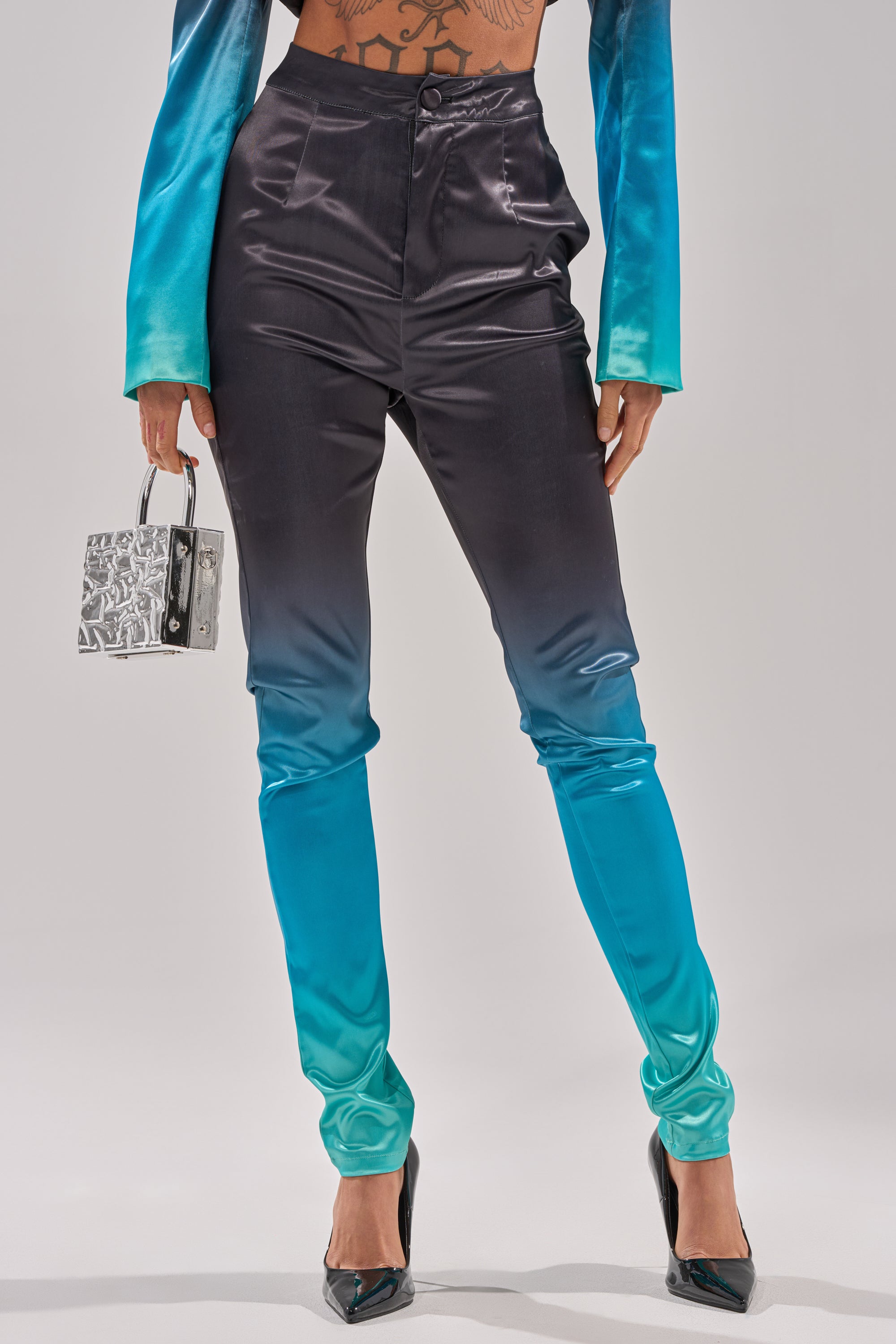 Wearing the NIGHT AND DAY OMBRE SKINNY TROUSER, which fades from black to bright blue, paired with a matching top, black heels, and a small metallic handbag. 2