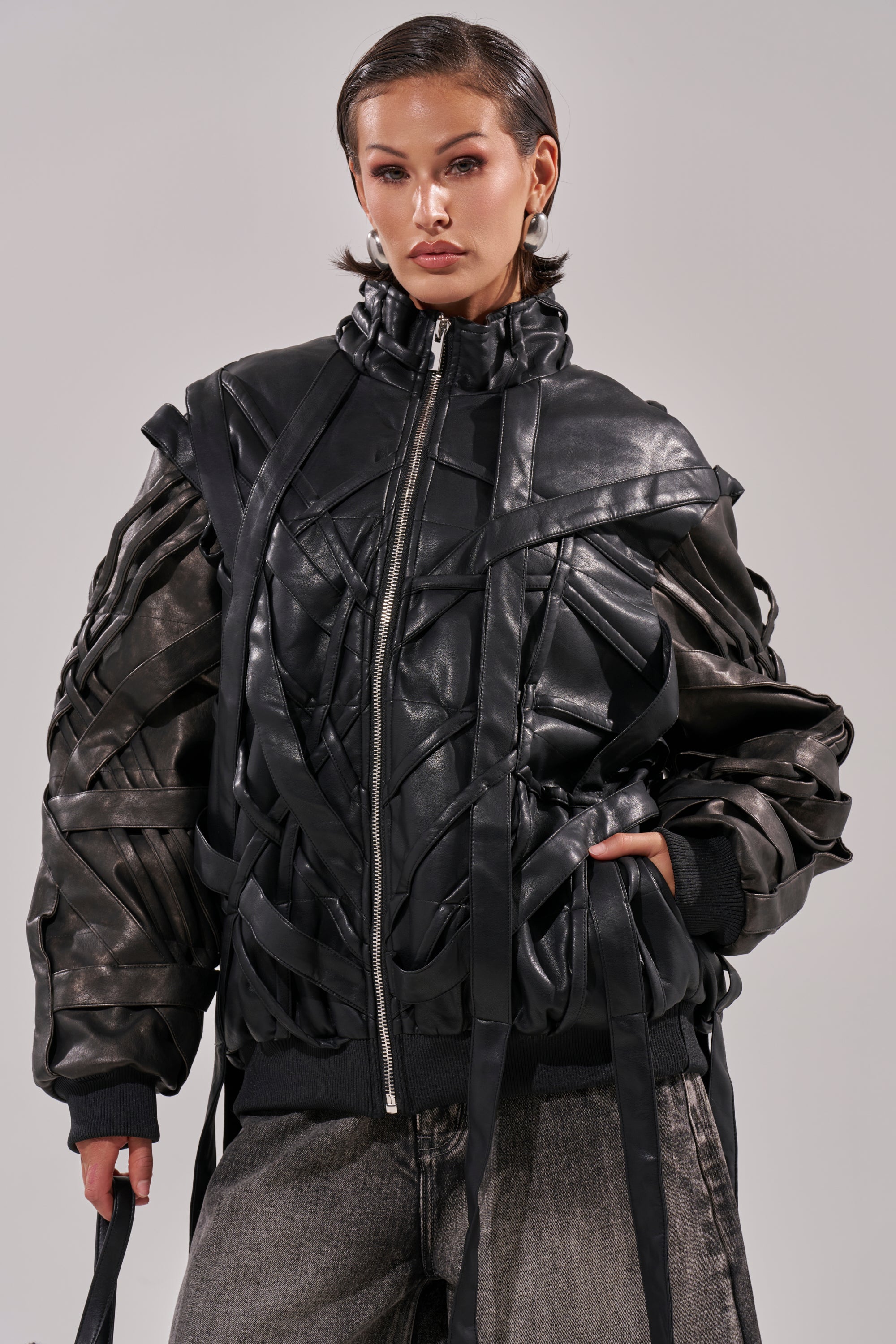 A woman in the LOCKED IN STRAP BOMBER, a sleek faux leather jacket. 0