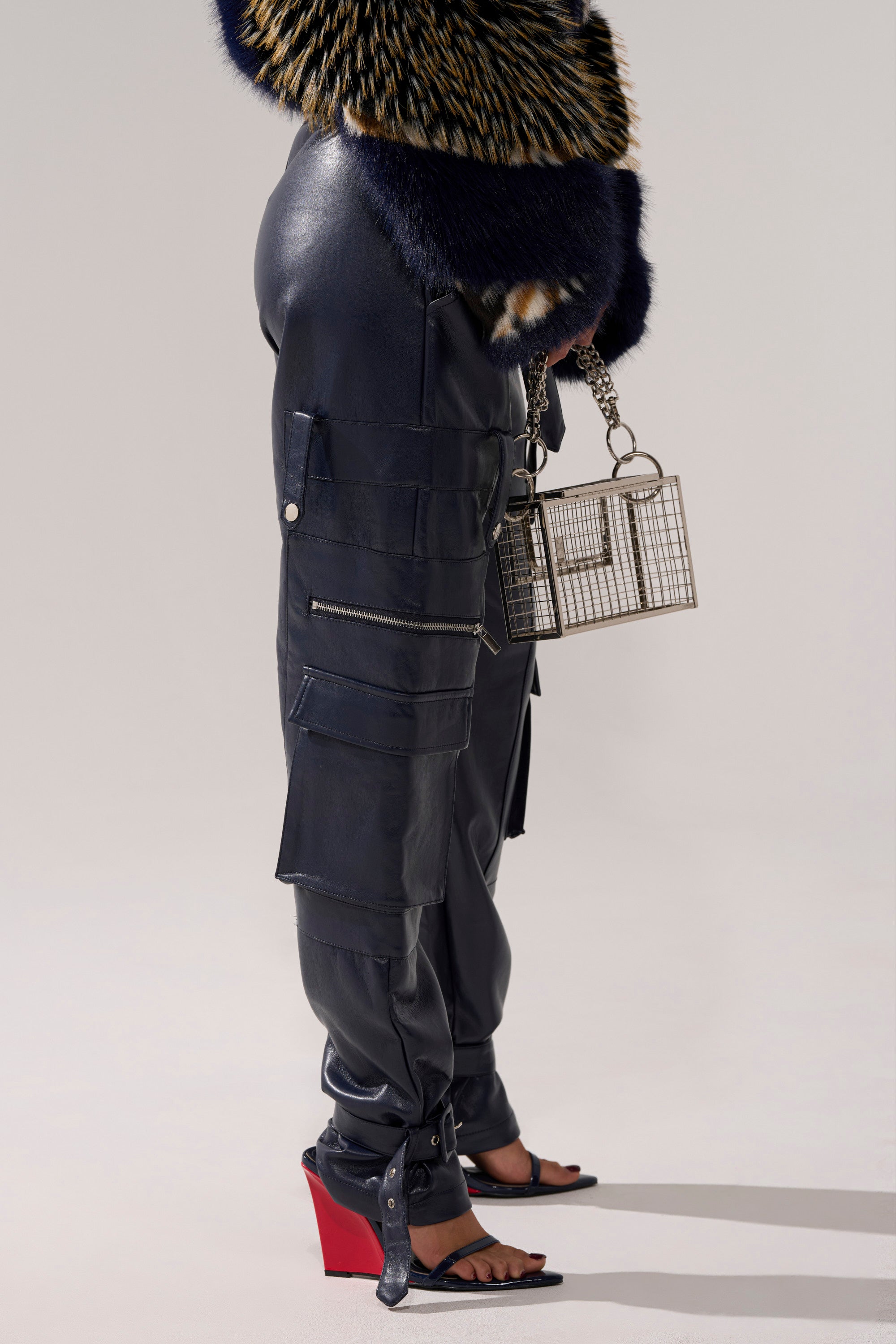 A person wears BUTTER LUXE PANTS IN NAVY, a multicolored faux fur top, black open-toe heels with red wedge soles, and holds a geometric metal handbag. The image is cropped at the shoulders.