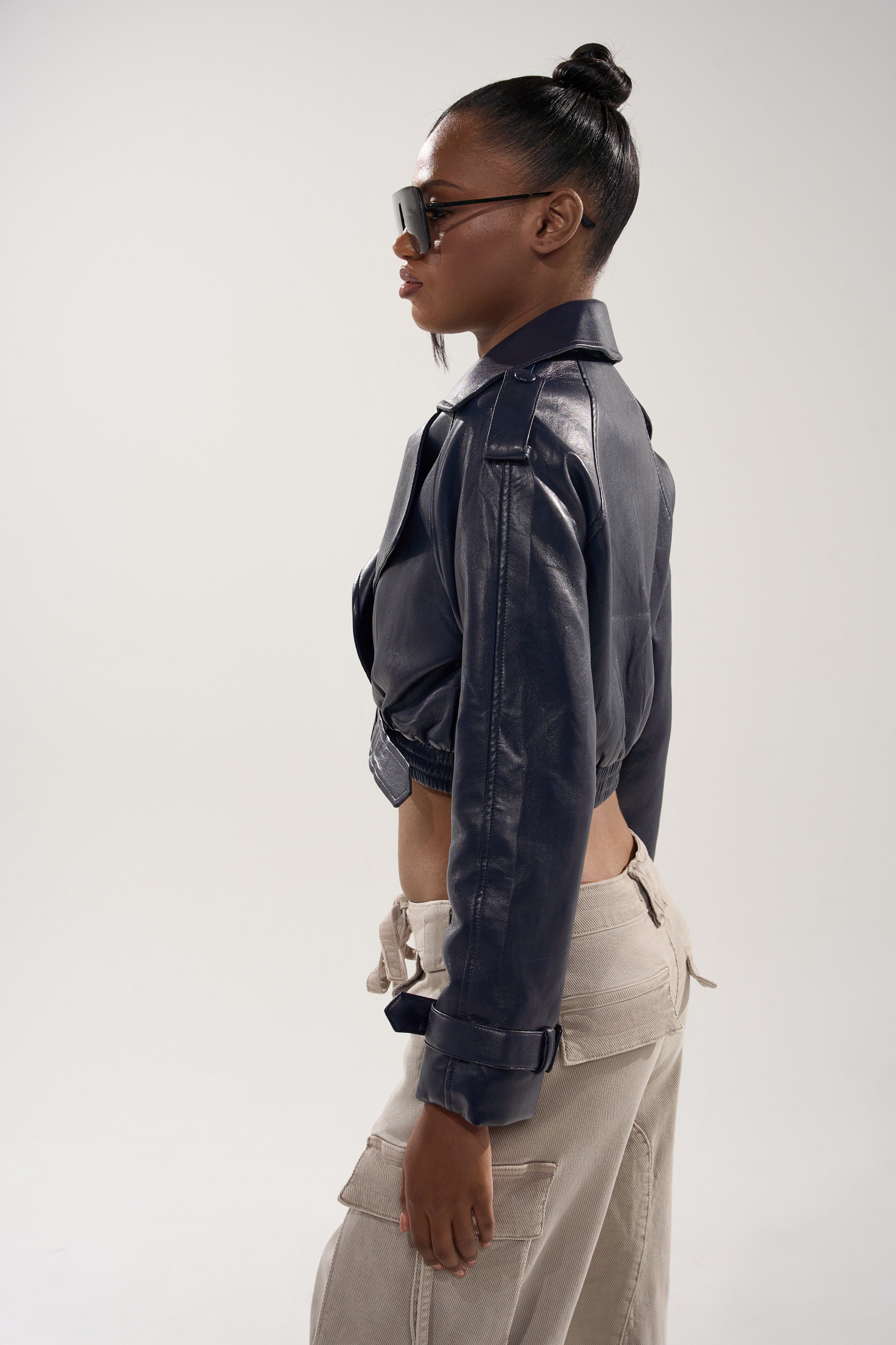 A woman in the BUTTER LUXE MOTO IN NAVY stands in profile, wearing sunglasses and beige cargo pants against a plain light background. 4