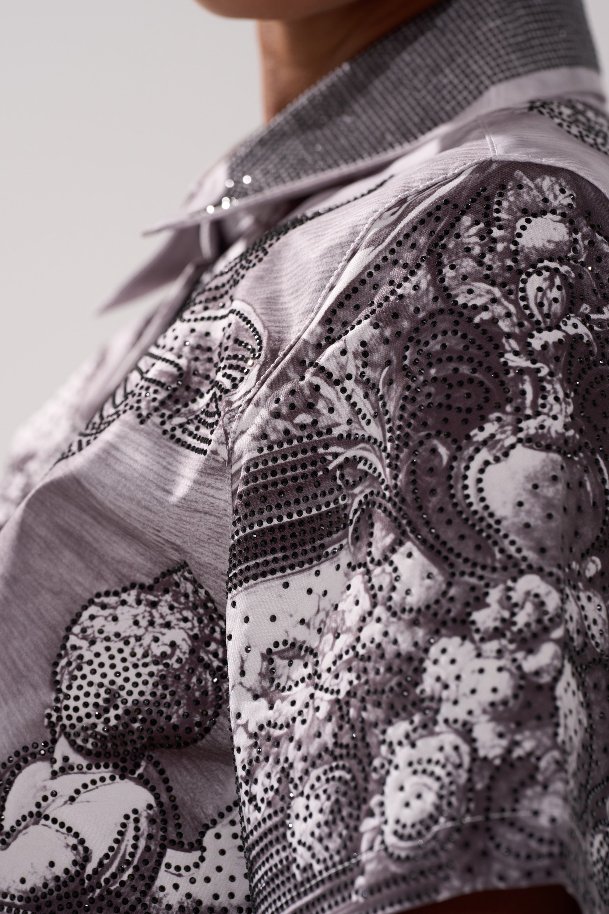 Close-up of a person wearing the FEELING ALL THE WAVES BUTTON DOWN, featuring intricate gray and white floral and dotted patterns. The focus is on the shirt’s textured details, with the face mostly out of frame.