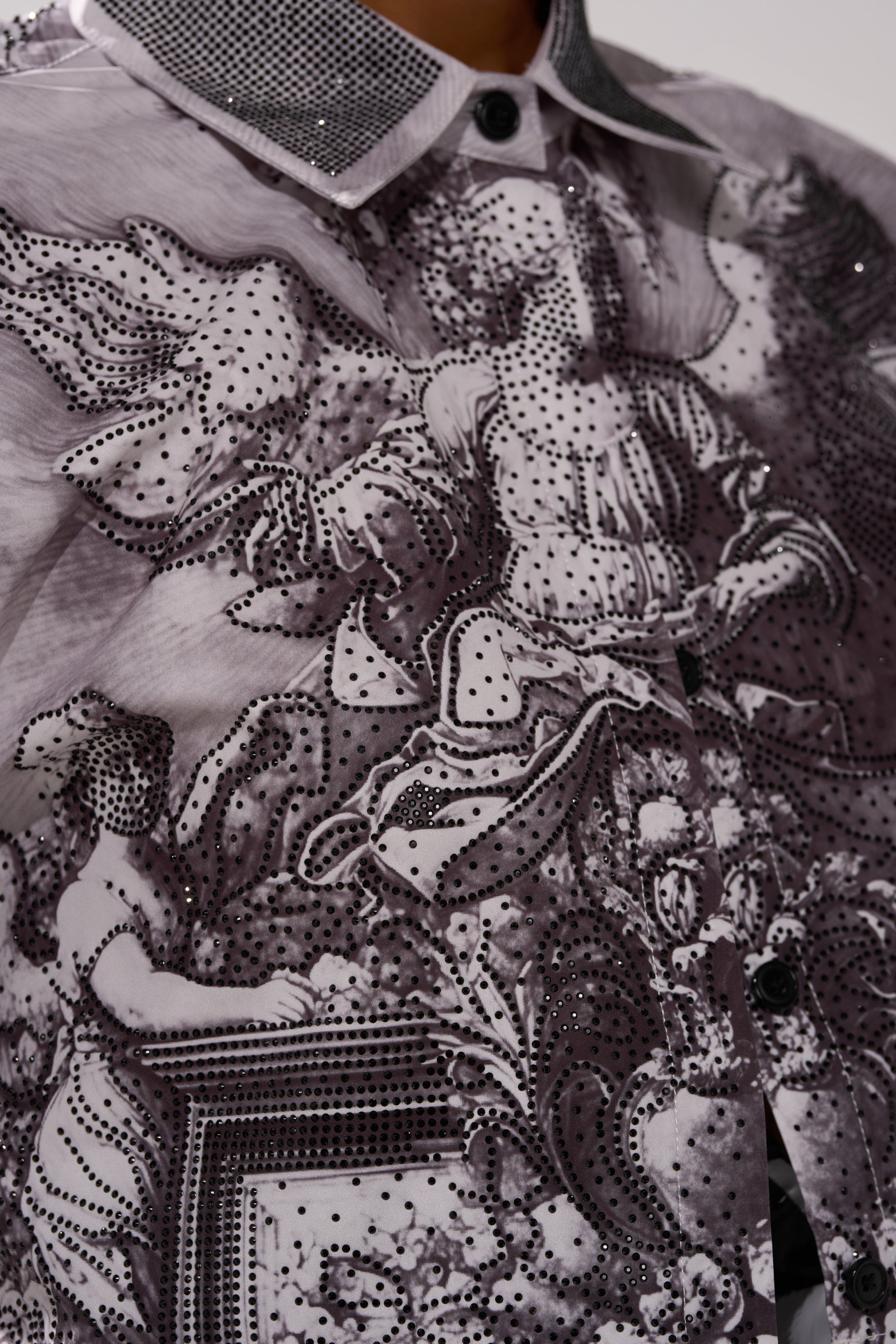 Close-up of the FEELING ALL THE WAVES BUTTON DOWN, a monochrome print shirt featuring intricate black-and-white classical figures, ornate designs, and small sparkling accents on sheer, finely detailed fabric.