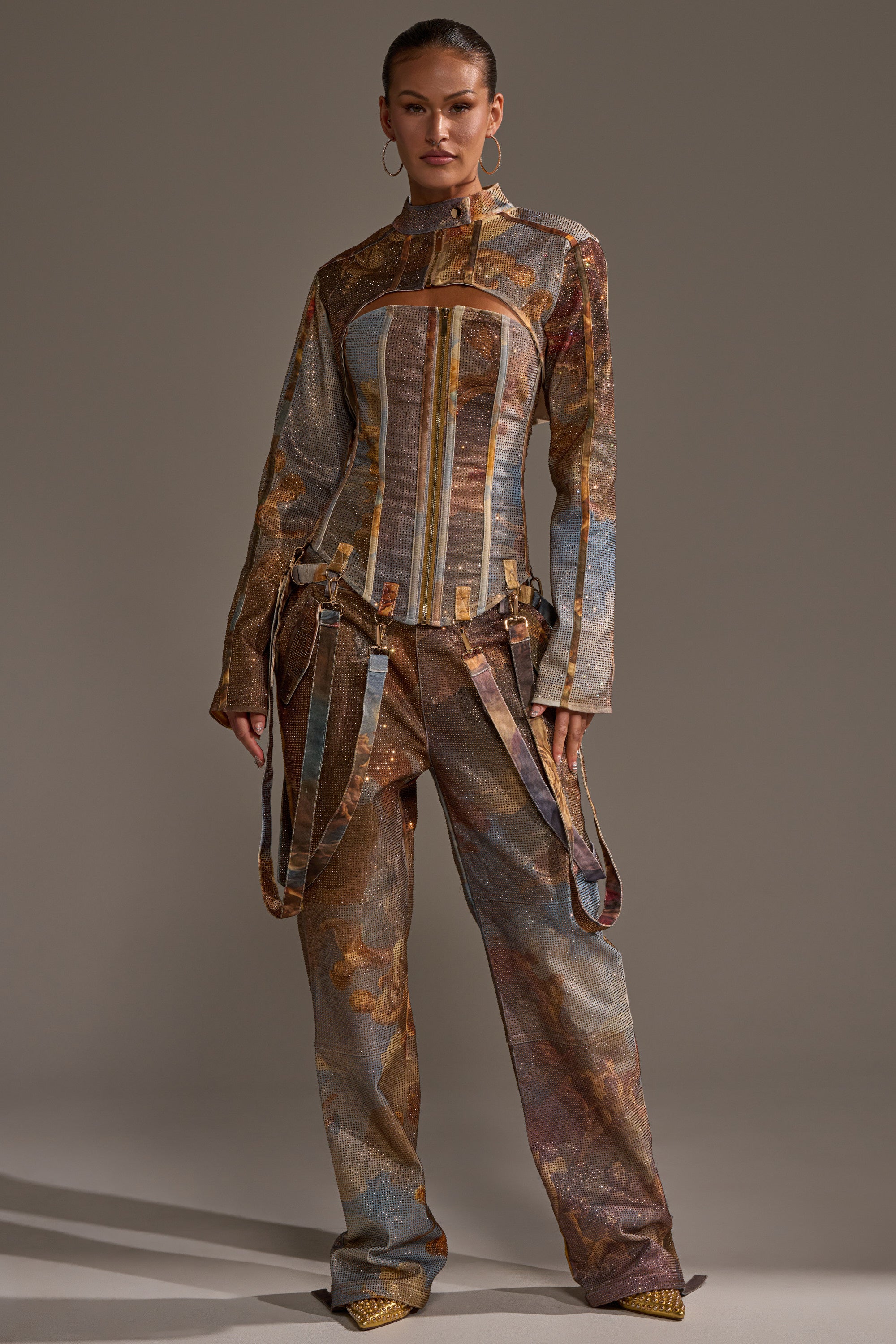 A woman stands confidently in the IN THE FUTURE RHINESTONE BOLERO, paired with earth-toned patterned pants and gold shoes, set against a neutral background.