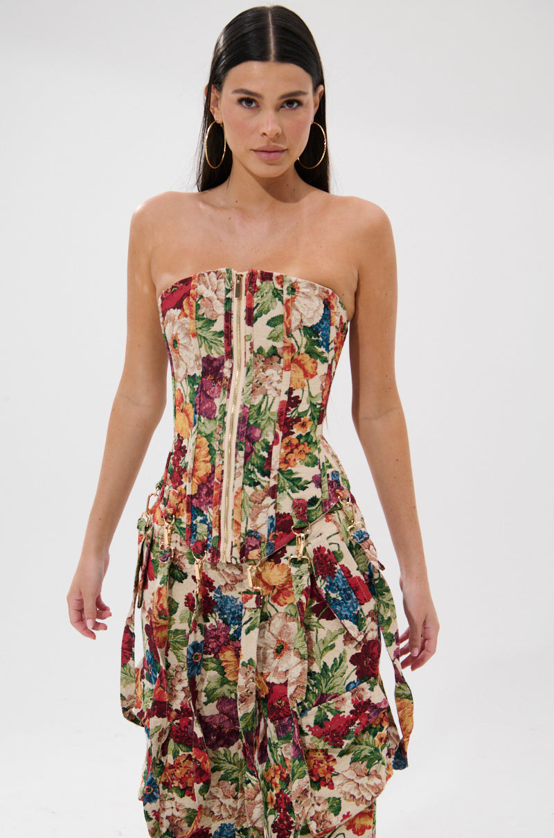 A woman with long dark hair models the FLORAL FOR DAYS BROCADE CORSET and matching pants, both in a vibrant multicolored floral brocade, standing against a plain white background.