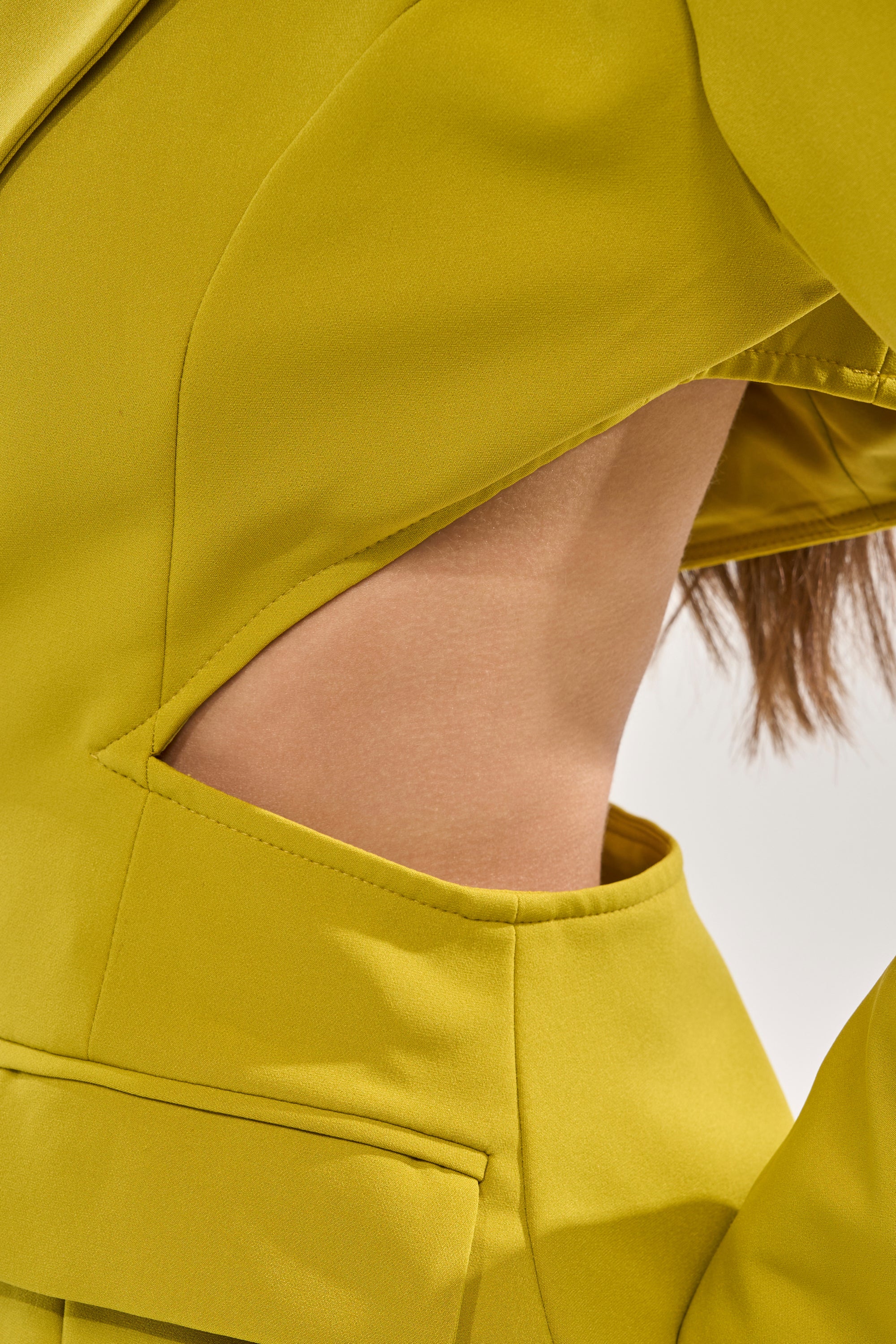 A close-up of someone in the PARTY IN THE BACK CUTOUT BLAZER IN CHARTREUSE, featuring smooth, structured fabric and bold waist cut-outs that reveal skin for a striking power-dressing look. 9