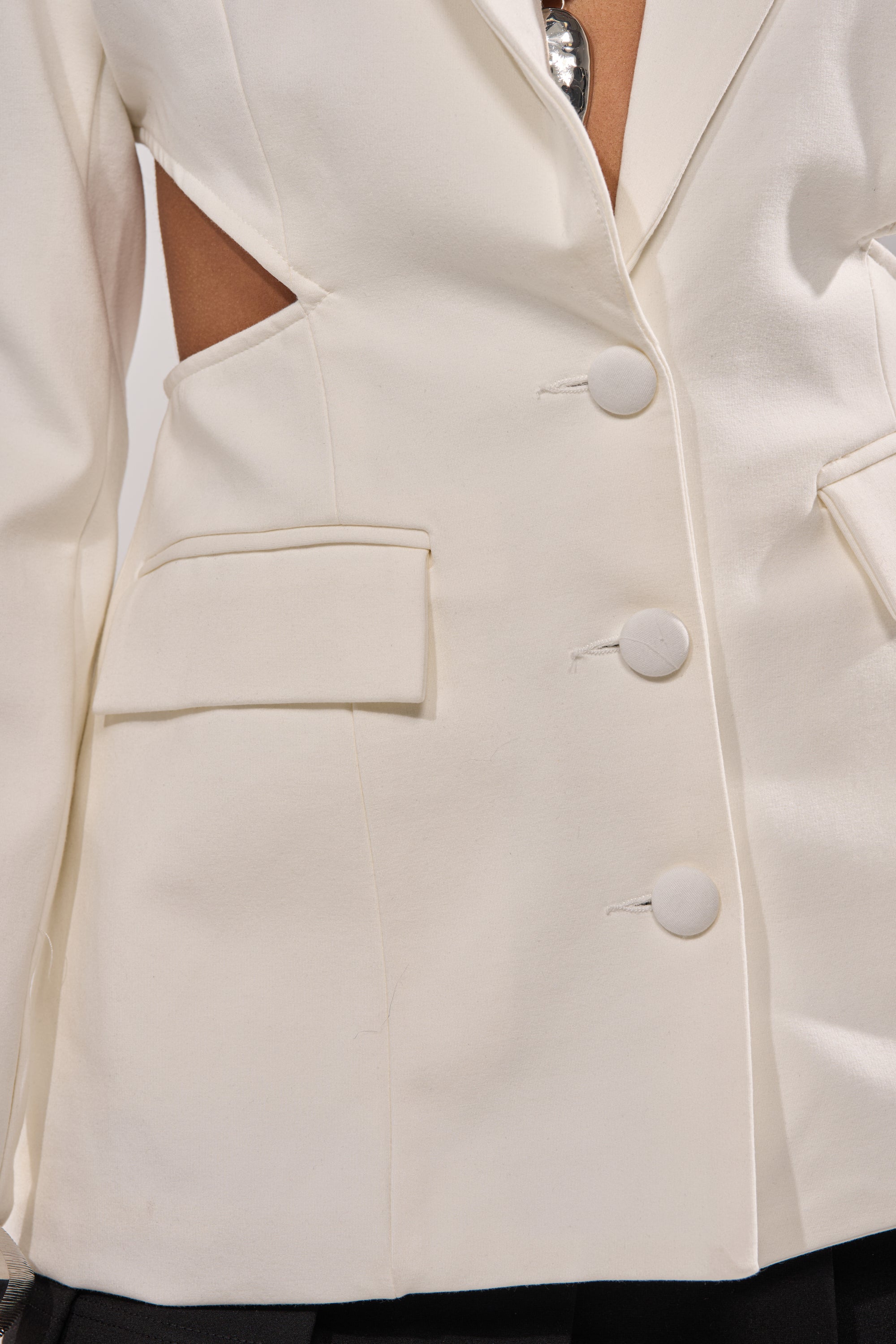 Close-up of the PARTY IN THE BACK CUTOUT BLAZER IN WHITE, featuring large buttons, flap pockets, and edgy side cut-outs in smooth structured fabric—a modern twist on classic office-wear. 7