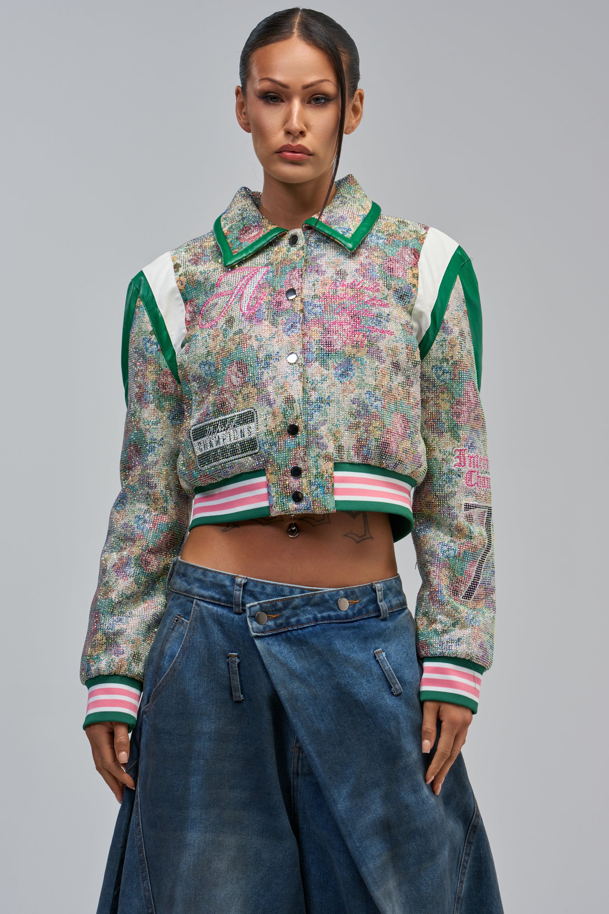 A person faces forward against a plain background, wearing the TAPPED OUT RHINESTONE BOMBER and wide-leg blue jeans with a double waistband and button detail.
