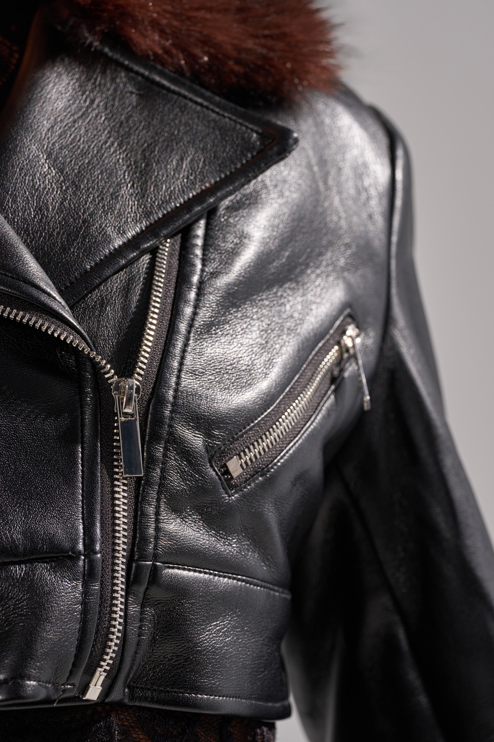 A close-up of the VICTORIA FUR TRIM MOTO, a black faux leather jacket with silver zippers, a wide lapel, and a dark brown fur collar for a luxe finish. 9