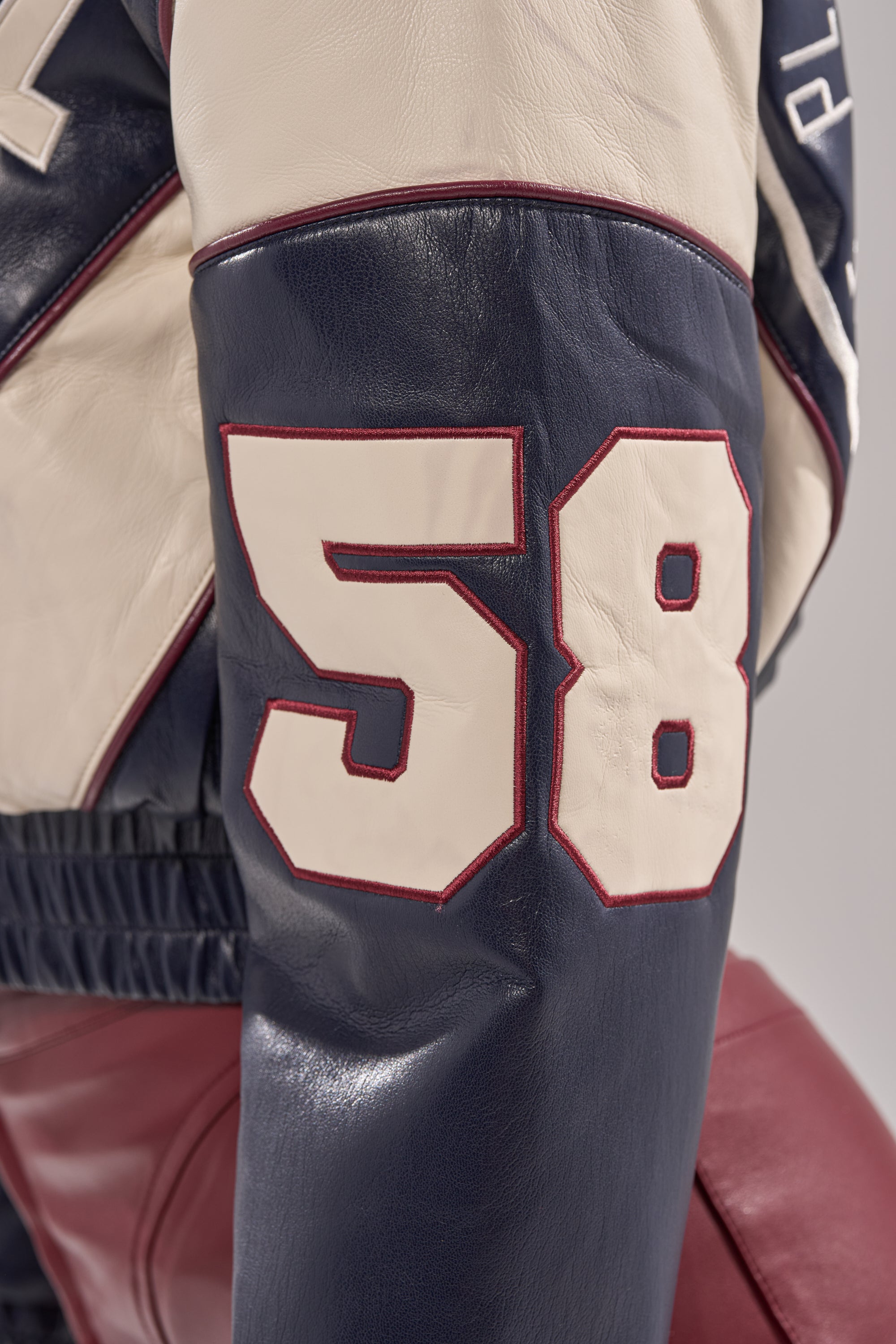 Close-up of the BUTTER LUXE VARSITY BOMBER's navy faux leather sleeve, featuring bold white and red-outlined 58, plus cream and maroon leather sections for a classic varsity style.