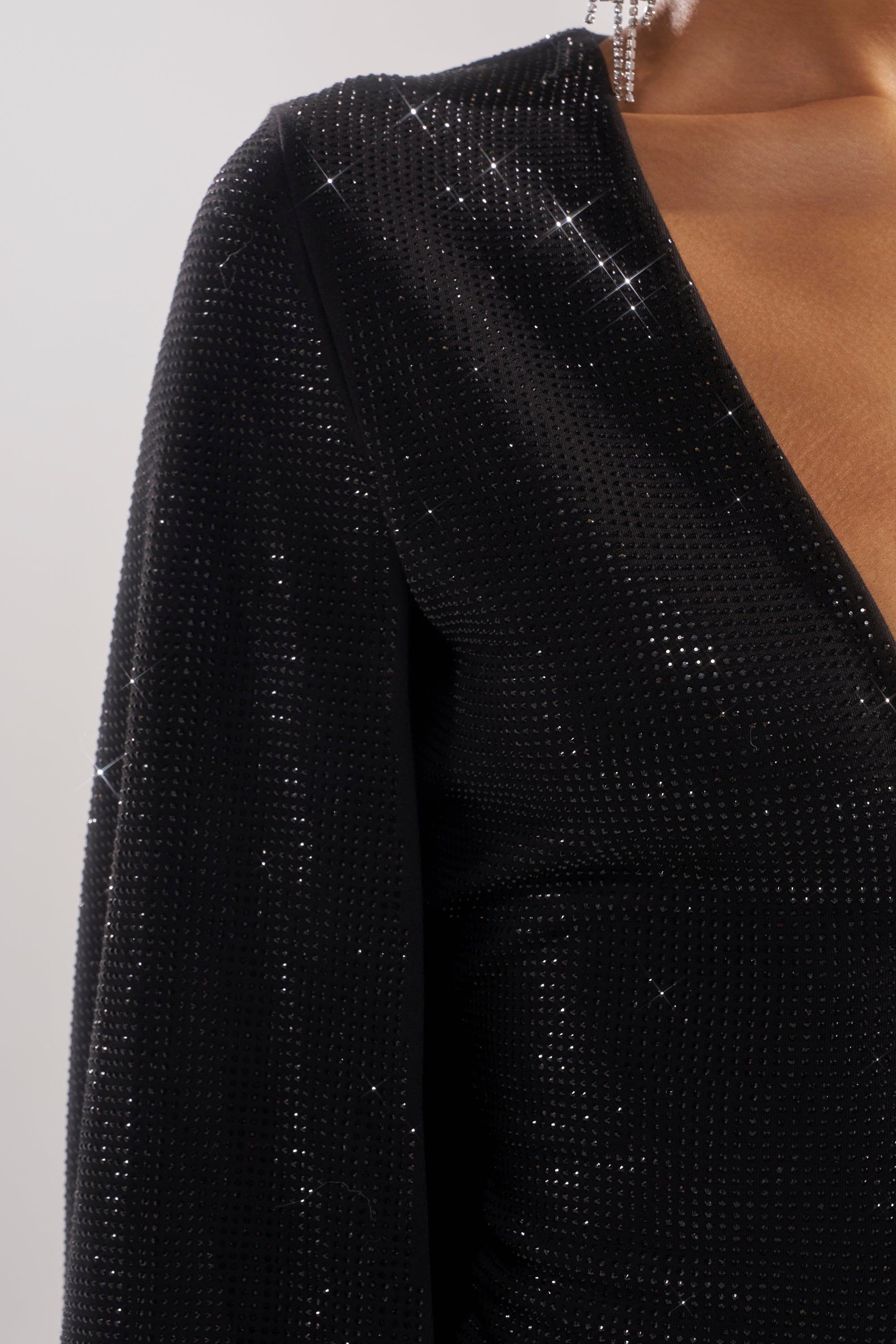 Close-up of a person wearing the LETS DANCE RHINESTONE MINI DRESS, featuring a glittering fabric, deep V-neckline, long sleeves, and dazzling rhinestone details. The bodycon mini dress stands out against a neutral background.