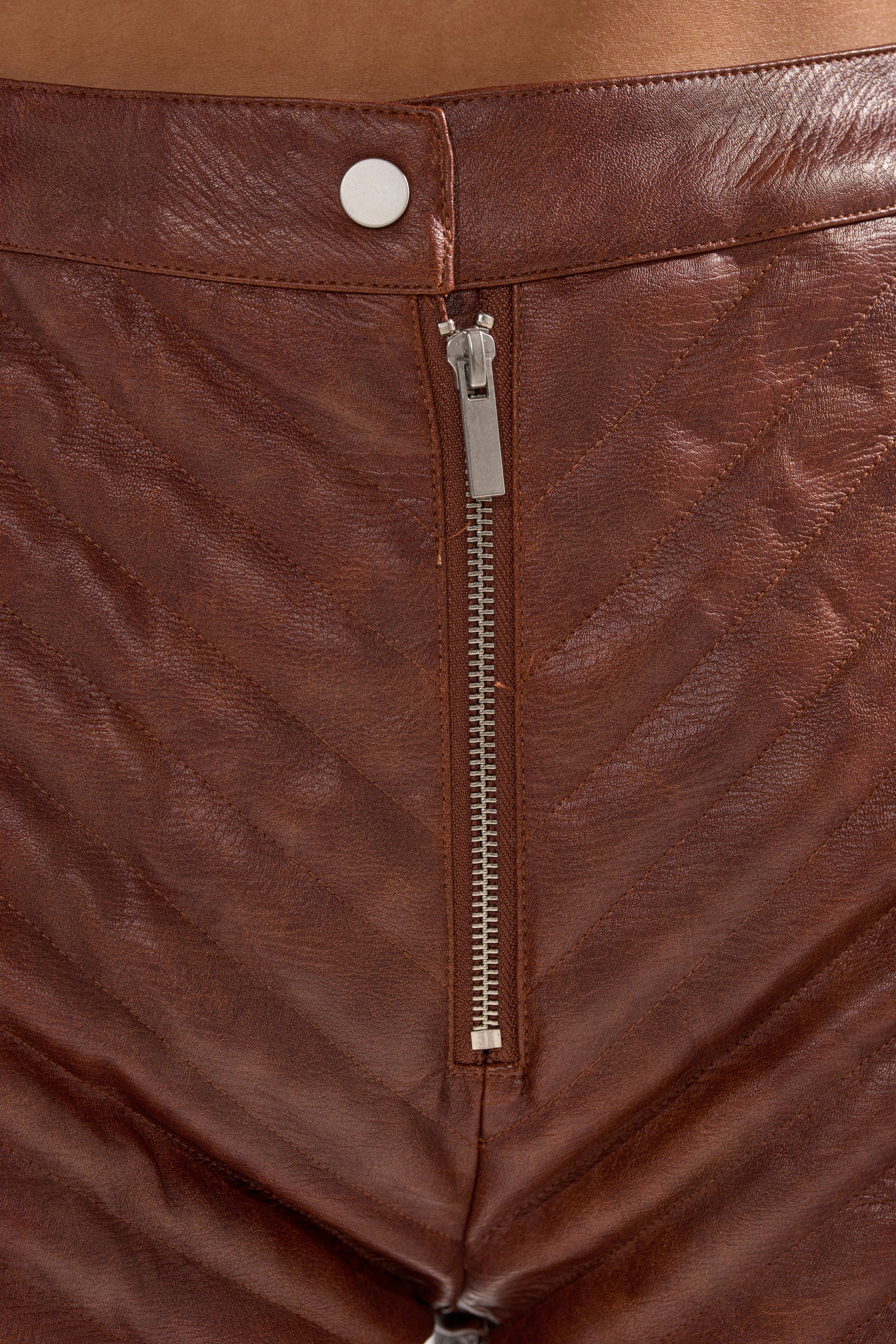 Close-up of the GALAXY FAUX LEATHER SHORT IN BROWN, showcasing a silver zipper, white waist button, and textured quilted design for a stylish look. 8