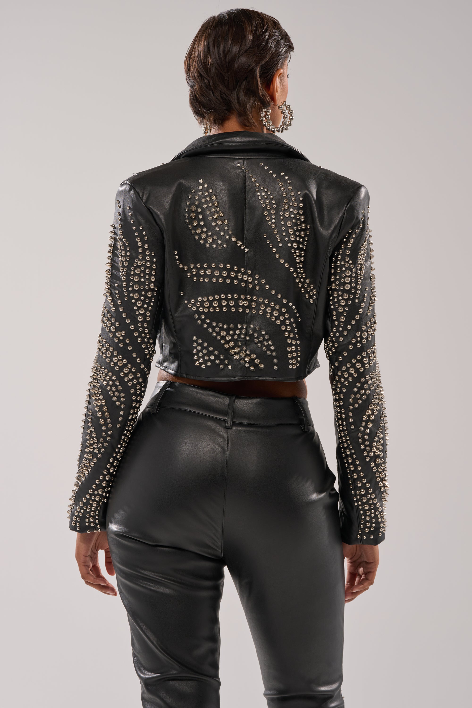 A person with short hair is seen from the back, wearing the GONE BAD STUDDED BLAZER—a black faux leather cropped blazer with silver studs on the sleeves and back. 4
