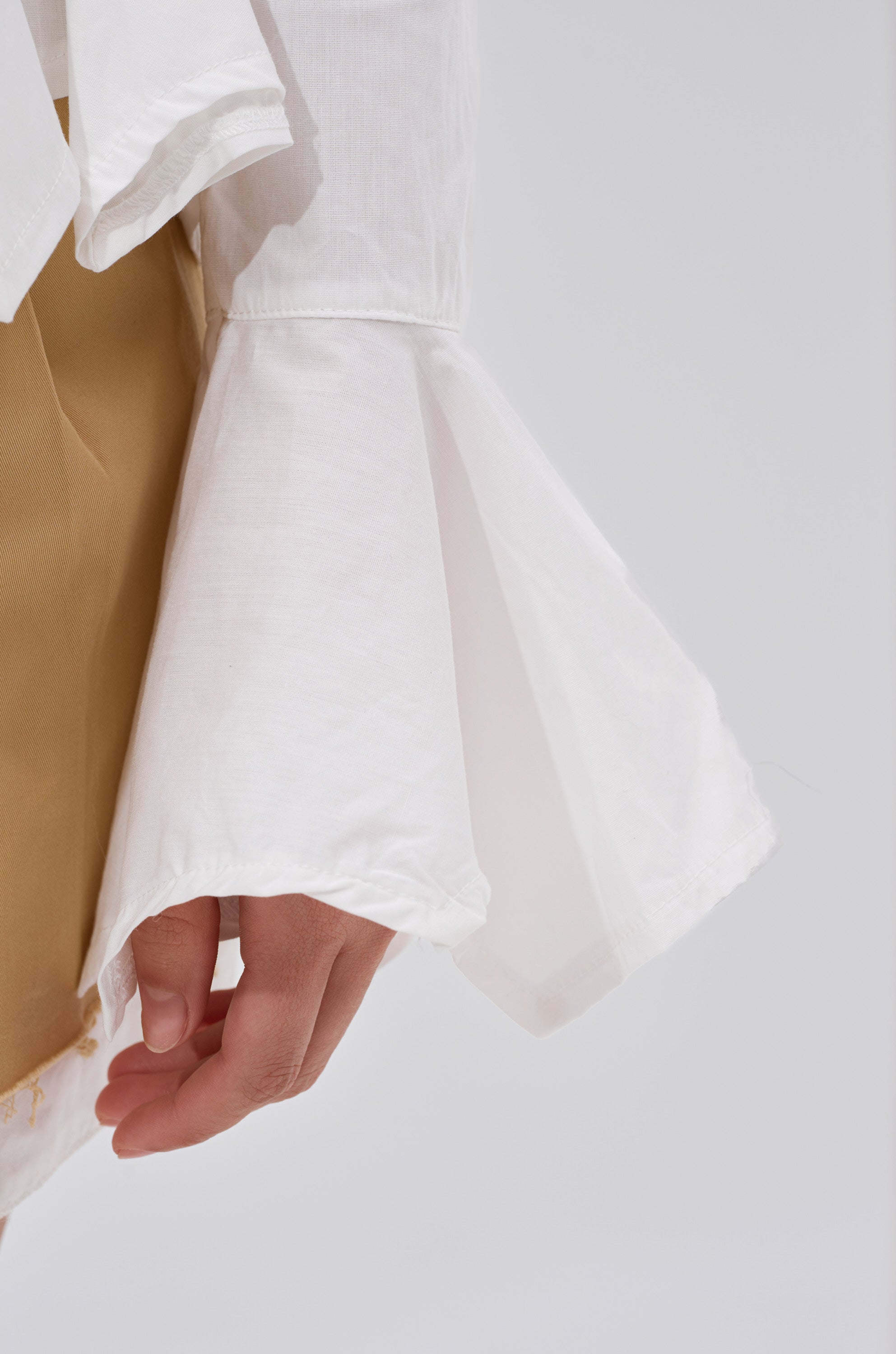 A person wears the ITS GOING TO BE ALRIGHT BUTTON DOWN, a white blouse with flared cuffs, paired with tan bottoms, shown from the waist down against a plain background with their hand relaxed at their side.