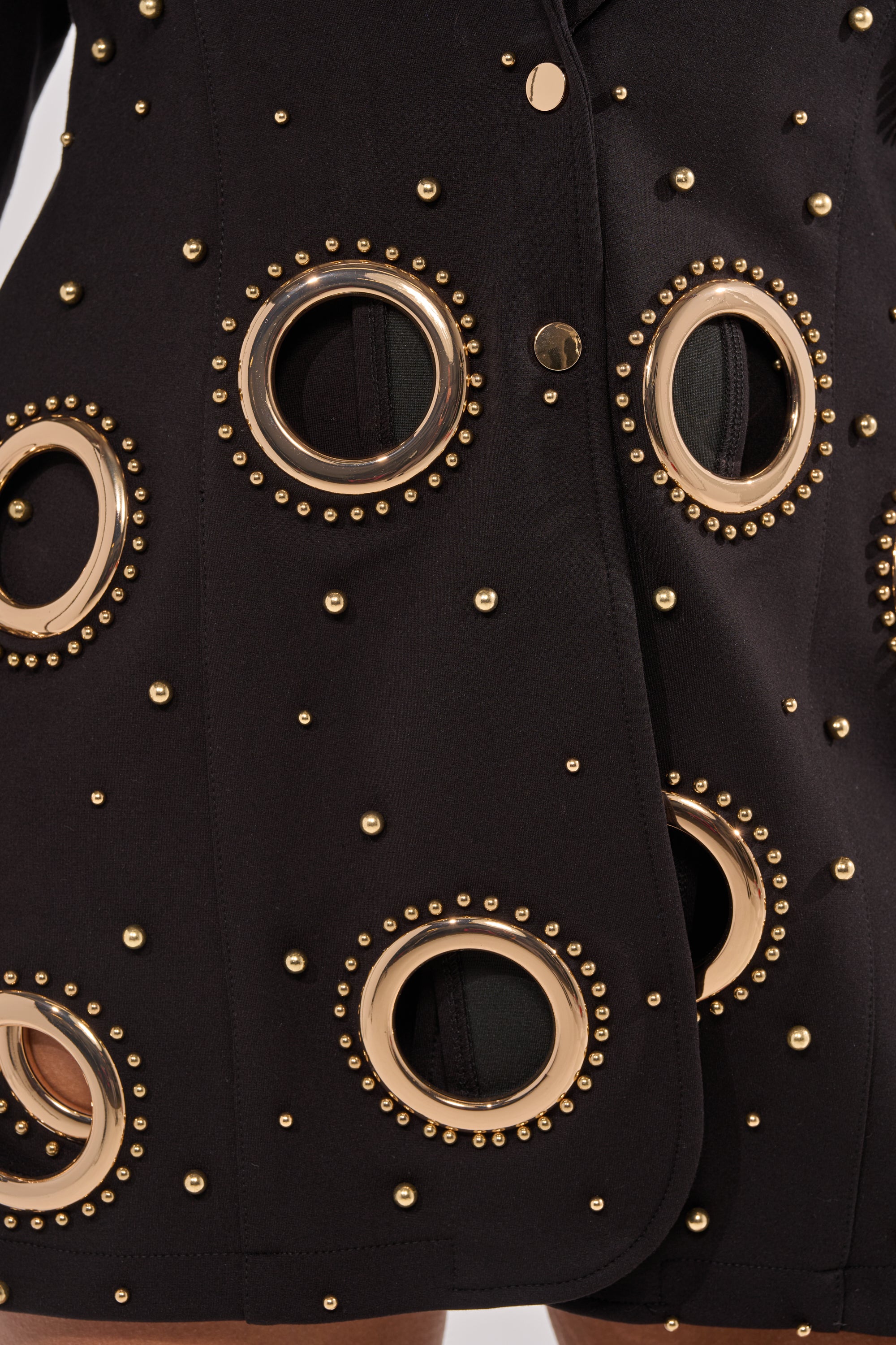 Close-up of the SHOW STOPPER BLAZER featuring a tailored silhouette, bold circular cutouts, large gold grommets, and gold-tone dome studs in a striking geometric pattern for a modern look. 11