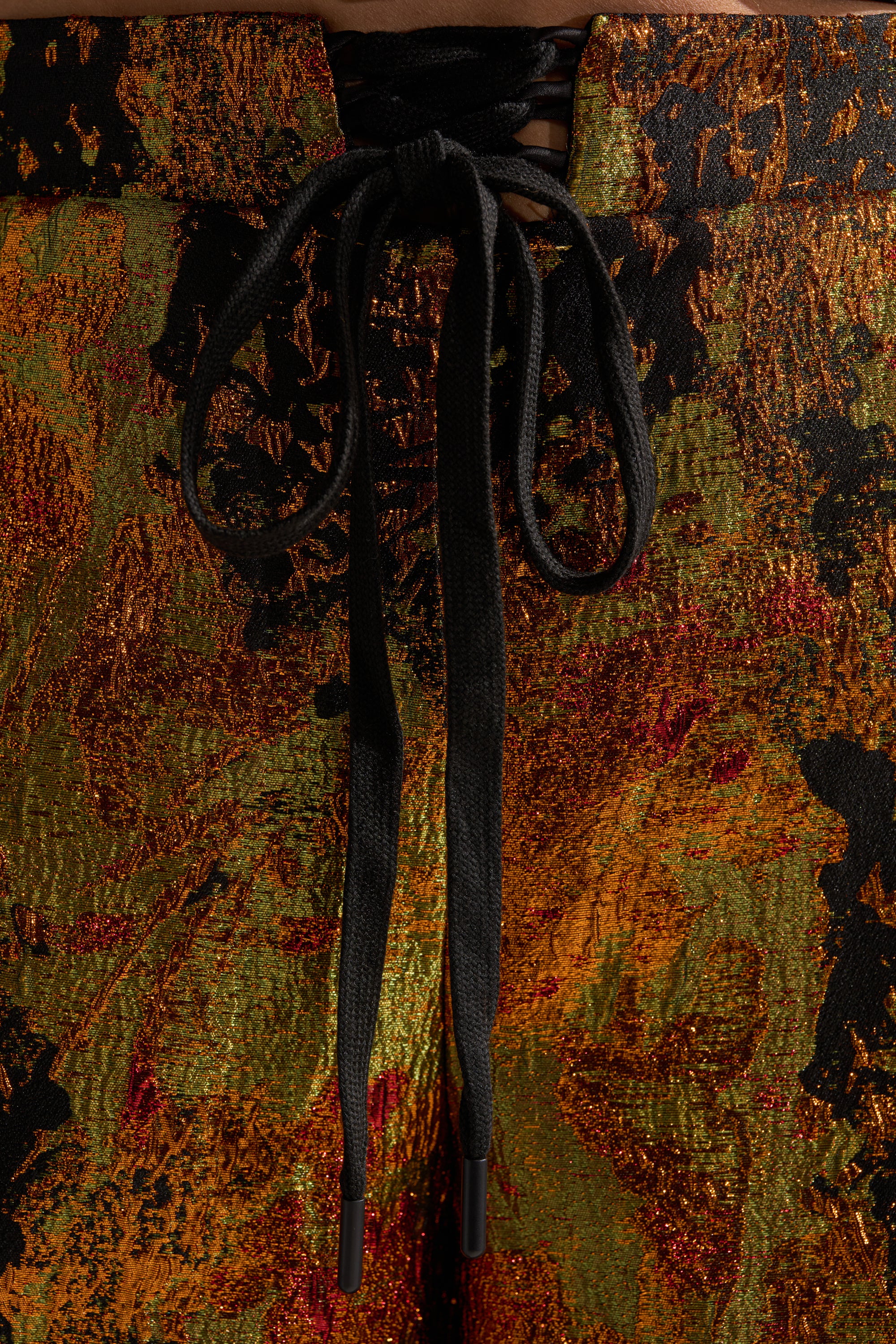 Close-up of TWIN FLAME BROCADE BERMUDA SHORTS featuring a vibrant gold, orange, and black abstract pattern with a front lace-up waistband tied in a bow for added style.