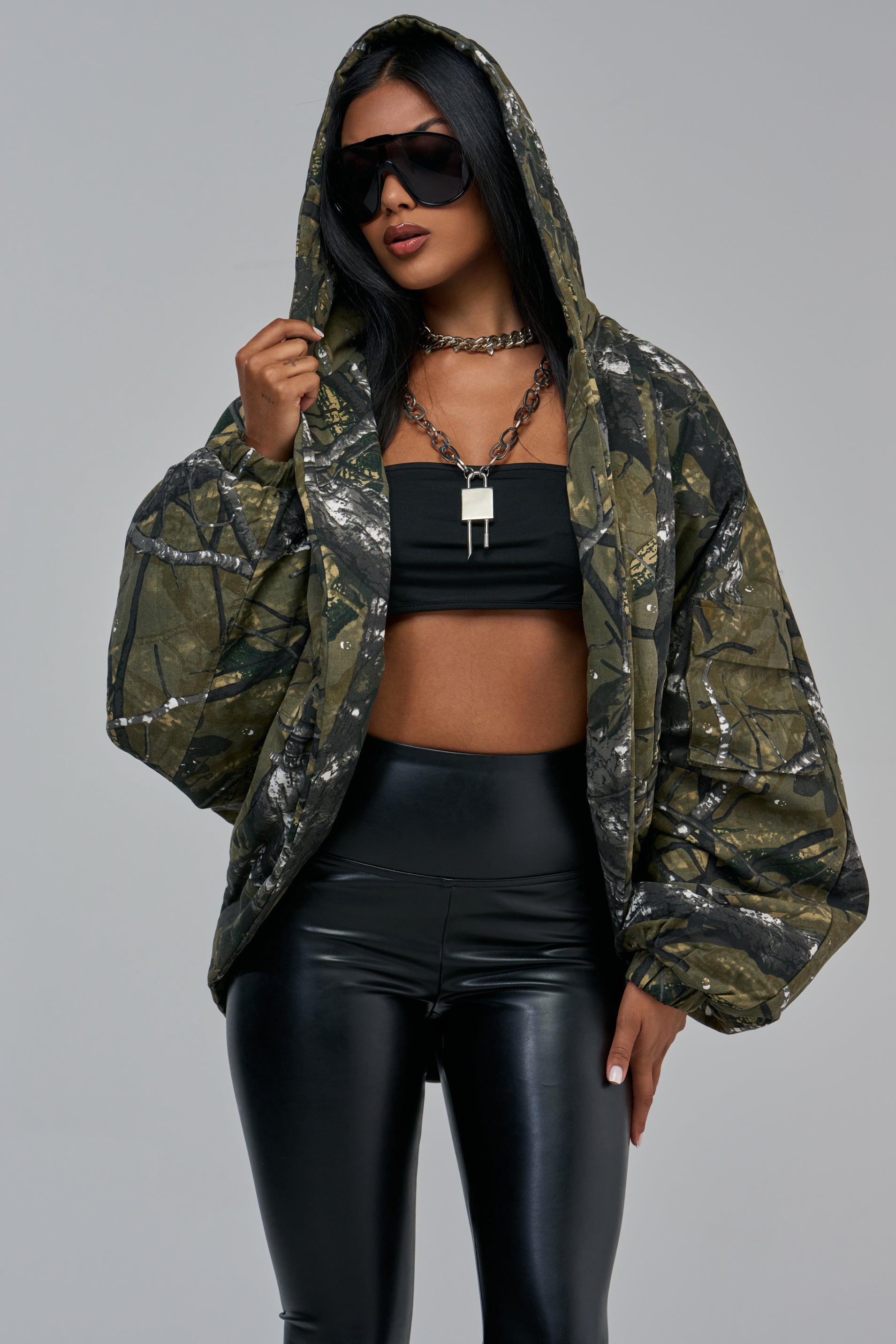 A person wearing an oversized INCONSPICUOUS CAMO COCOON JACKET with the hood up, a black tube top, and black leggings for a classic fall layering look.