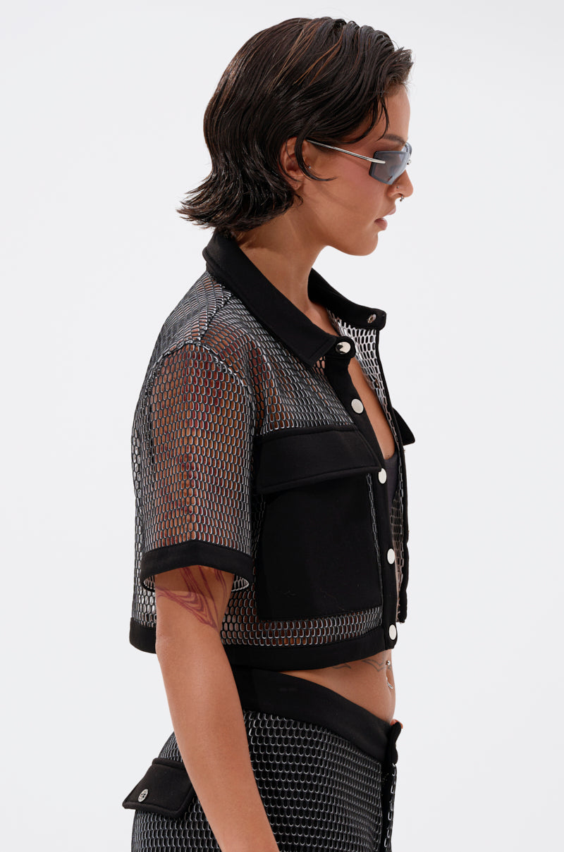 A person with short, wet-look hair wears futuristic sunglasses and the STEPHANIA TRANSPARENT BUTTON DOWN, a black fishnet mesh short-sleeve jacket with large pockets and button details, shown from the side against a plain background.