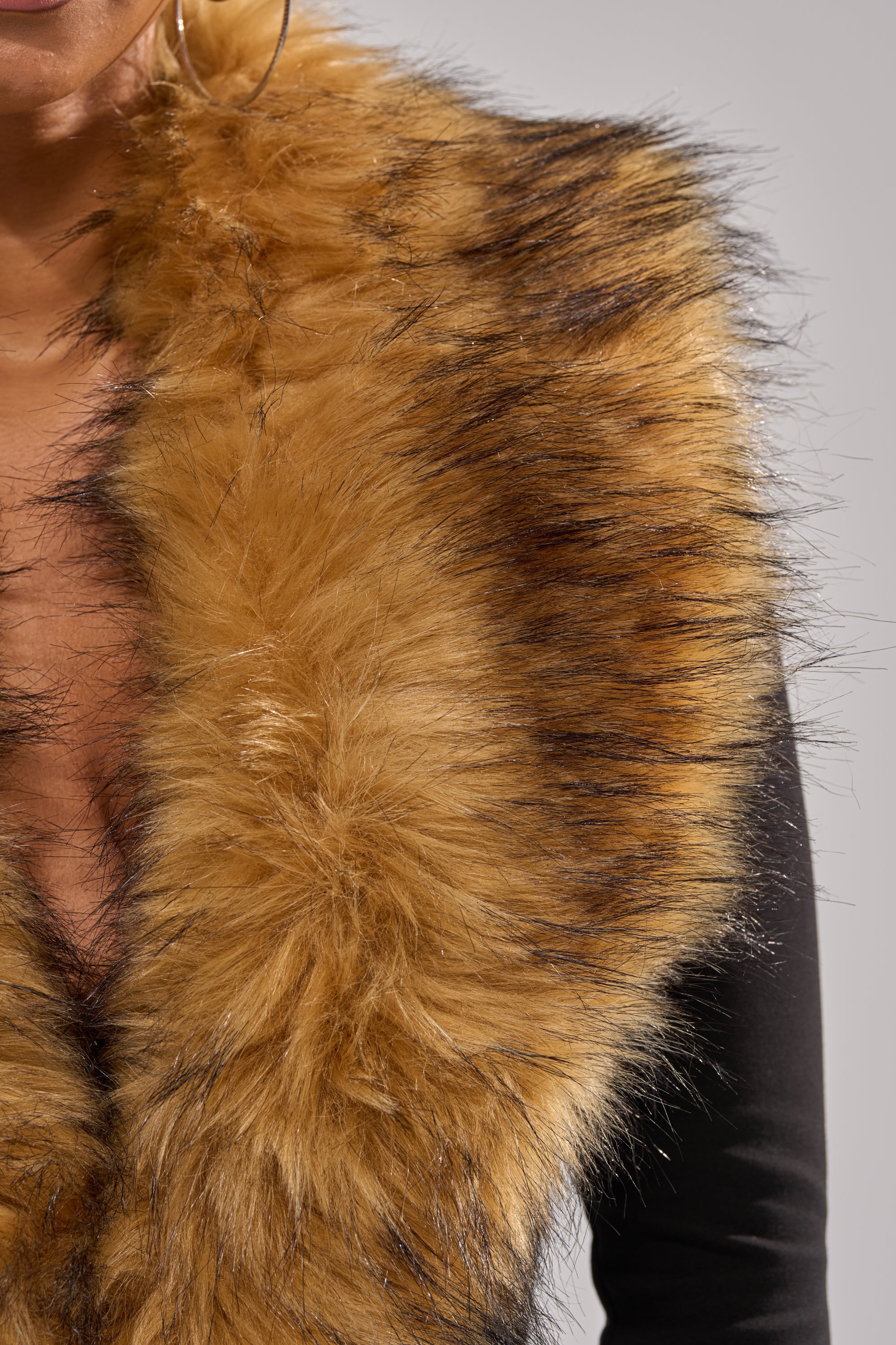 A close-up of a person wearing the OH HOT DAMN BABY FUR TRIM JUMPSUIT with a luxurious golden brown and black-tipped faux fur trim, showing only the lower face, neck, and shoulders. Perfect for a stylish holiday party look.