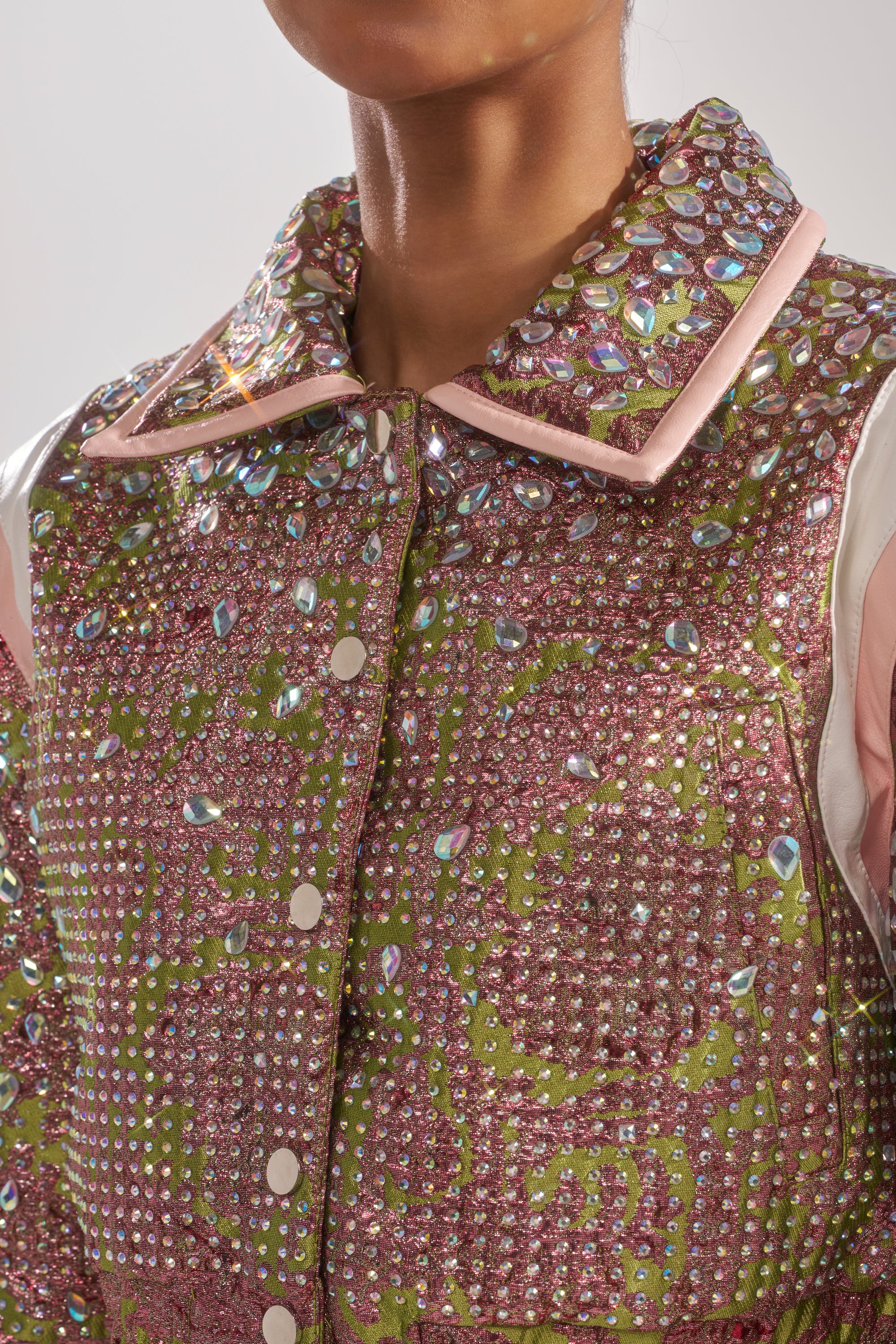 A close-up of a person wearing the TIME AND TIME AGAIN RHINESTONE BOMBER, a cropped jacket featuring sparkling sequins and colorful pink, green, and white gem patterns with shiny embellishments on the collar and front. 9