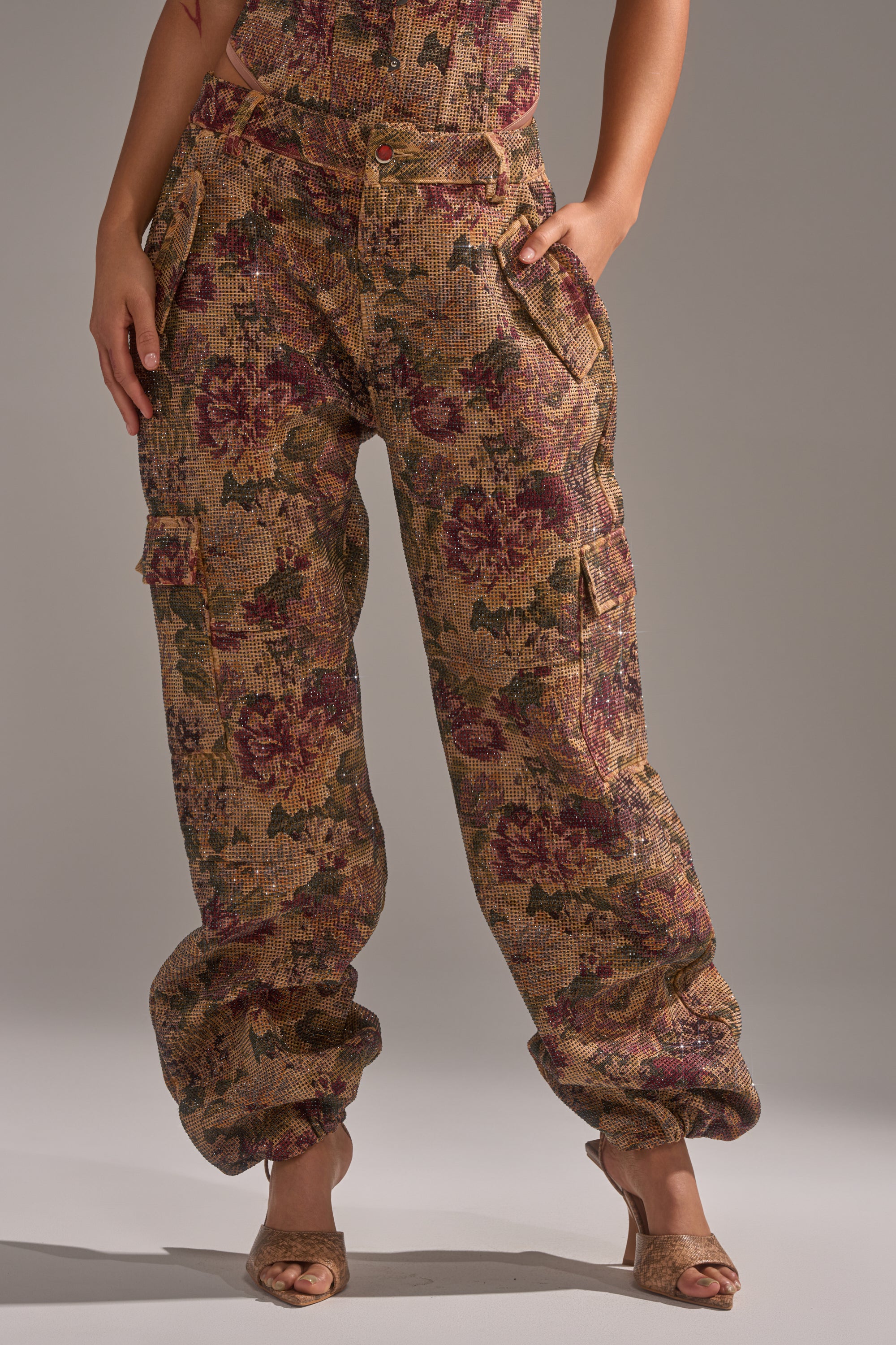 A person wears the GLAM SQUAD RHINESTONE BROCADE TROUSER—loose, high-waisted brown and pink pants with a wide-leg silhouette, side pockets, and textured floral jacquard fabric—perfectly paired with open-toe heels. 2