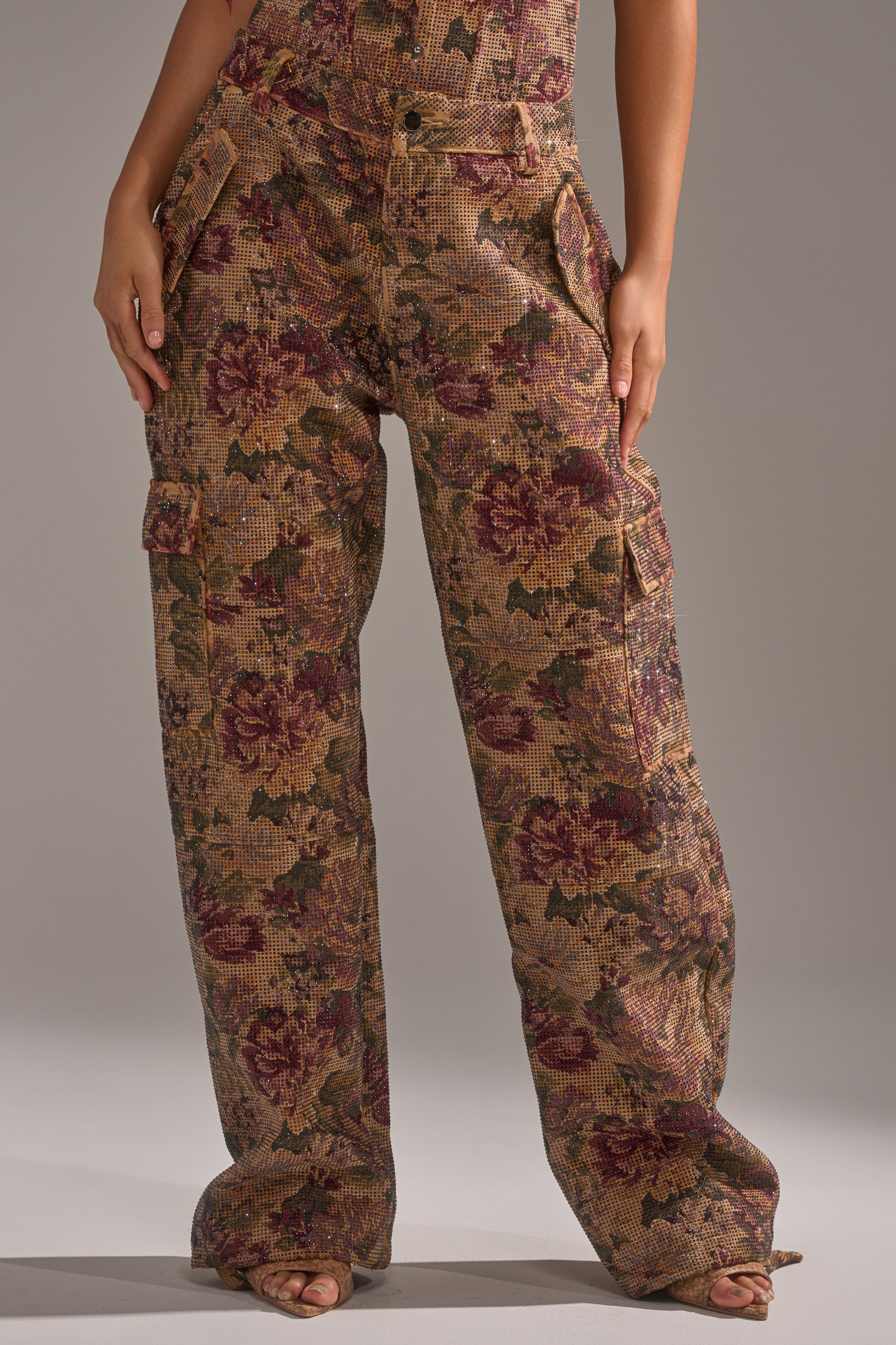 A person wearing the GLAM SQUAD RHINESTONE BROCADE TROUSER—high-waisted, wide-leg brown and burgundy floral jacquard pants—stands with hands in pockets, lower body only visible. 3