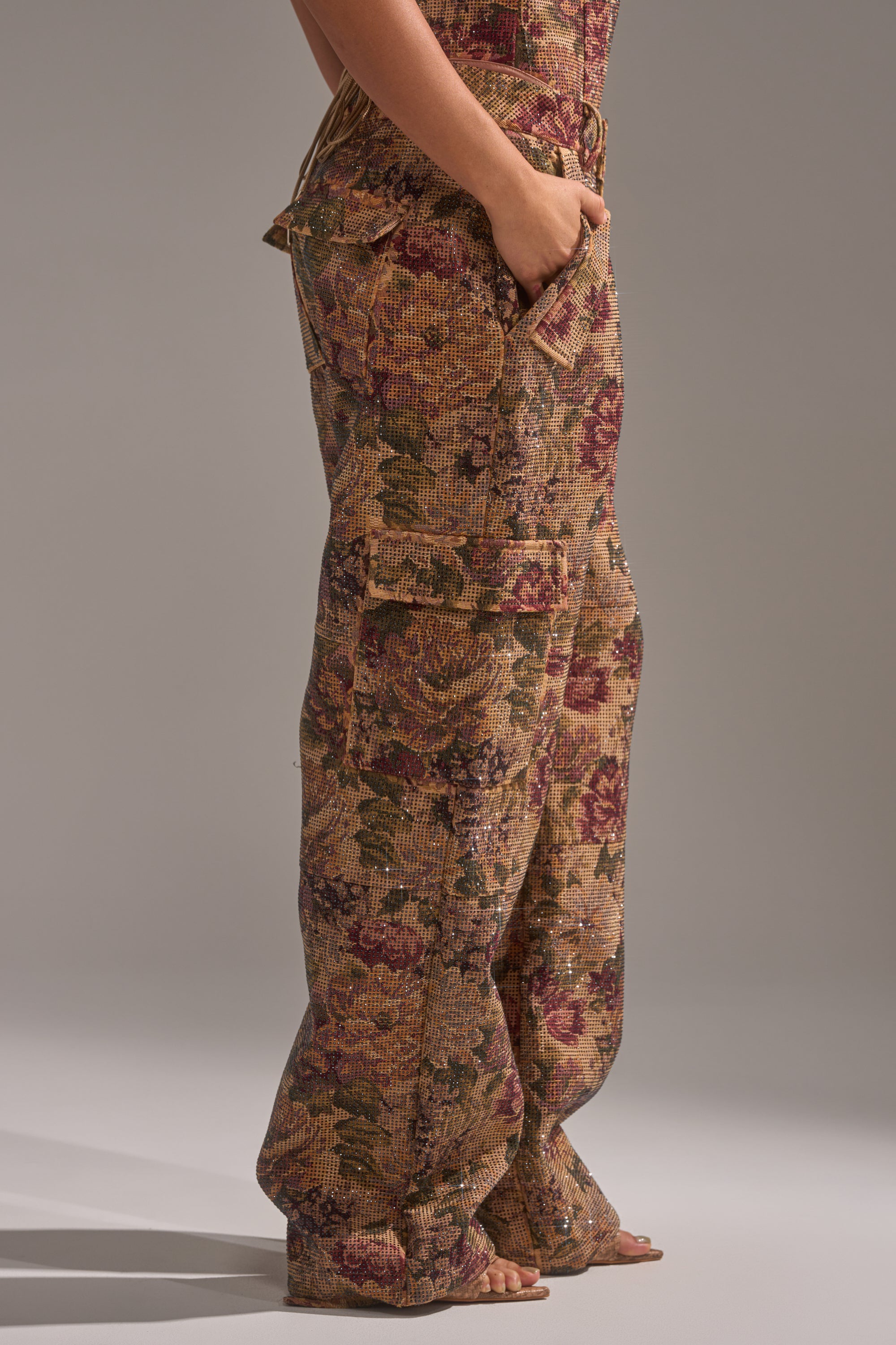 A person stands sideways with one hand in the pocket of the GLAM SQUAD RHINESTONE BROCADE TROUSER; the photo is cropped above the waist, emphasizing the loose, floor-sweeping silhouette and intricate brocade detailing. 4