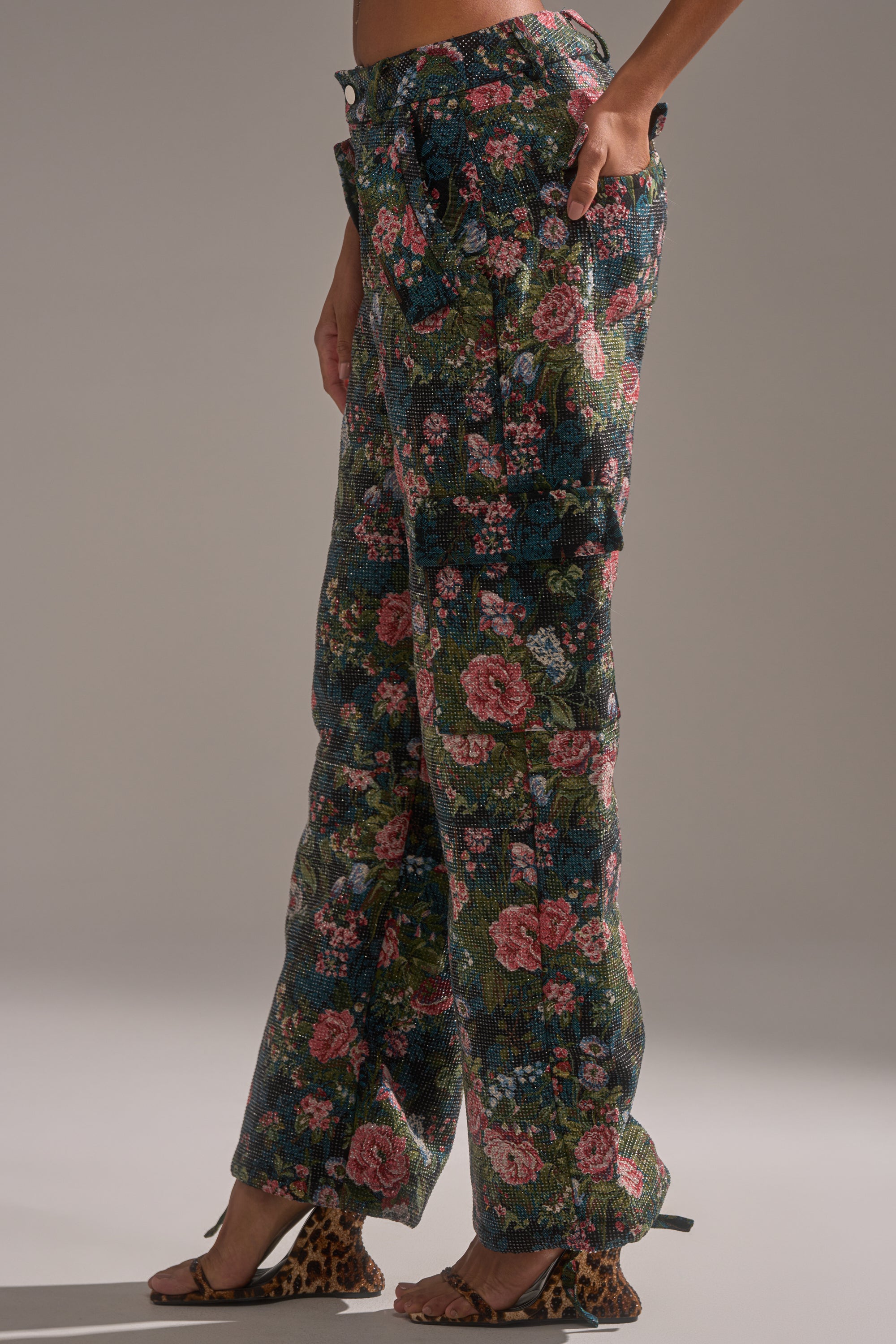 Wearing the I WANT YOU FLORAL RHINESTONE TROUSER with buttoned pockets and open-toe leopard print heels creates a bold statement look against a plain, neutral background.