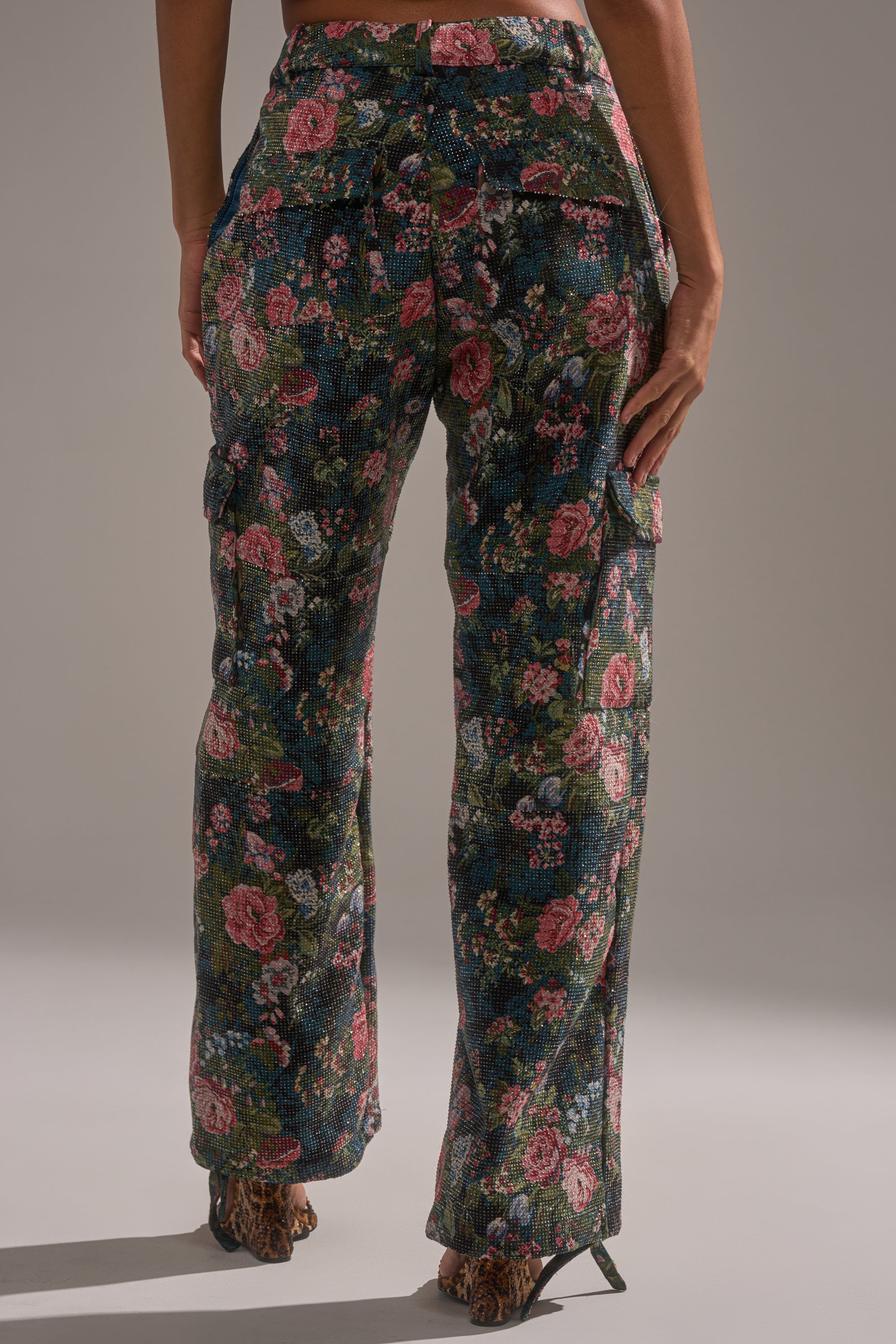 A person is seen from the back wearing the I WANT YOU FLORAL RHINESTONE TROUSER—high-waisted with a vibrant floral print—standing on a light surface, ideal for making a bold statement.