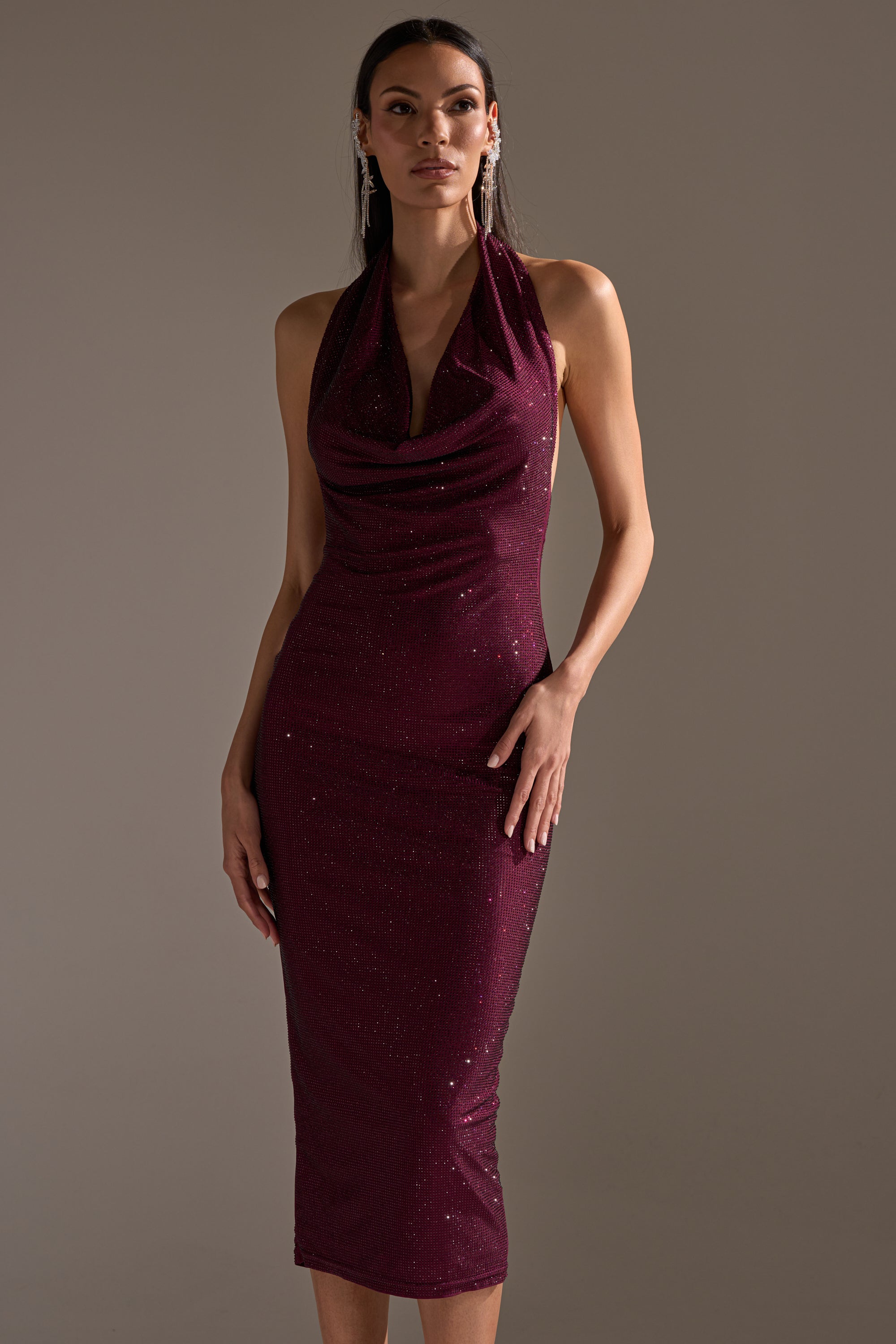 A woman poses in the POPPIN' BOTTLES RHINESTONE MAXI DRESS IN PURPLE—a sleeveless, sequined halter-neck dress that falls below the knee—standing against a neutral background with one hand on her hip.
