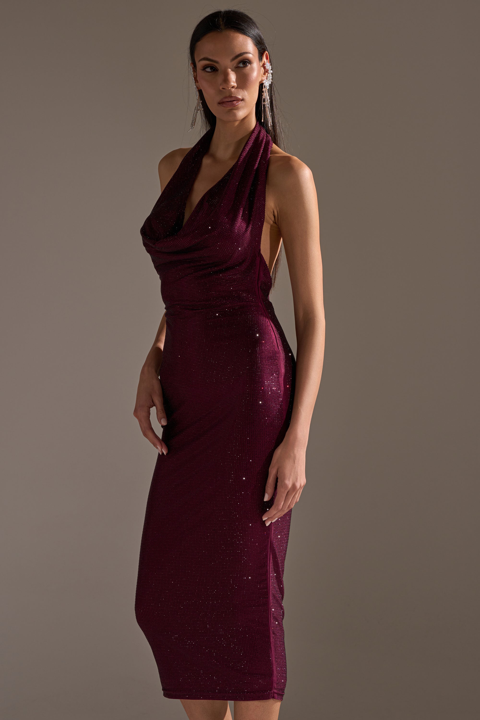 A woman models the POPPIN' BOTTLES RHINESTONE MAXI DRESS IN PURPLE, a sleeveless halter maxi with a draped neckline and shimmering rhinestone details, exuding party-ready glamour against a simple neutral backdrop.