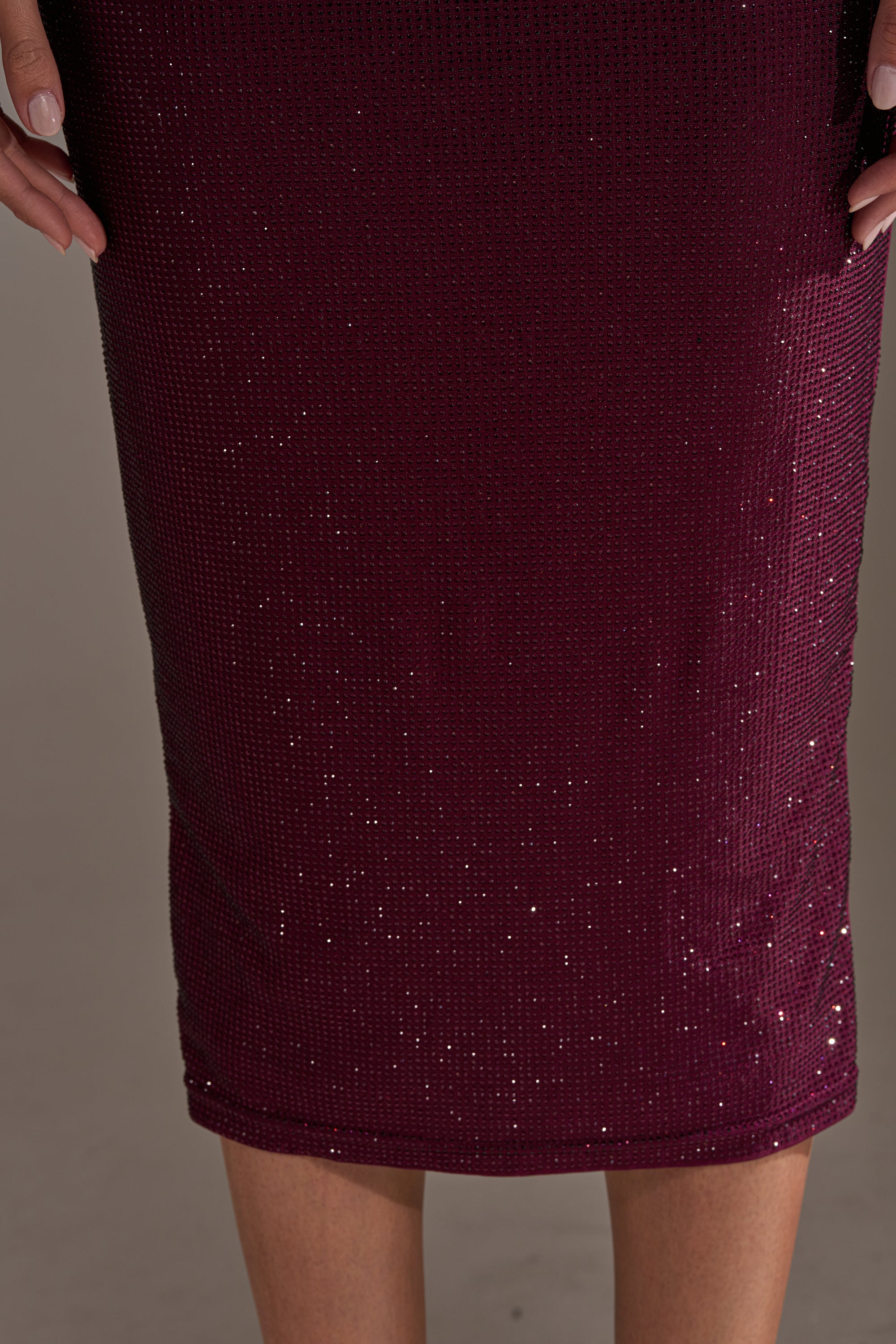 A close-up of a person wearing the POPPIN' BOTTLES RHINESTONE MAXI DRESS IN PURPLE. The sparkling, curve-hugging skirt catches the light, while their hands rest near the top edges against a softly blurred background.