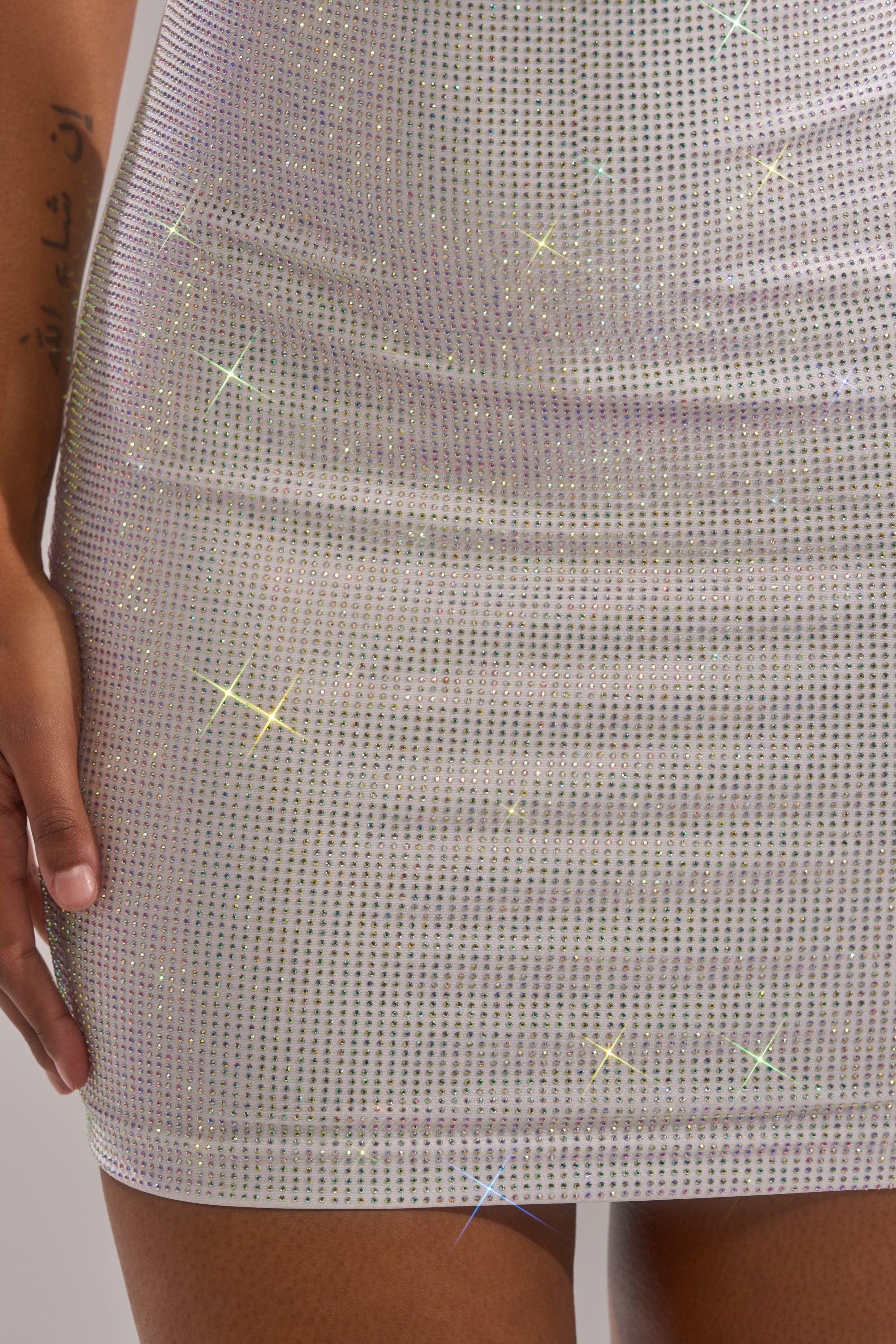 A close-up of a person wearing the COCKY AF Rhinestone Snake Mini Dress in White, with their left hand at their side and star-like rhinestone reflections shimmering across the dress. 8