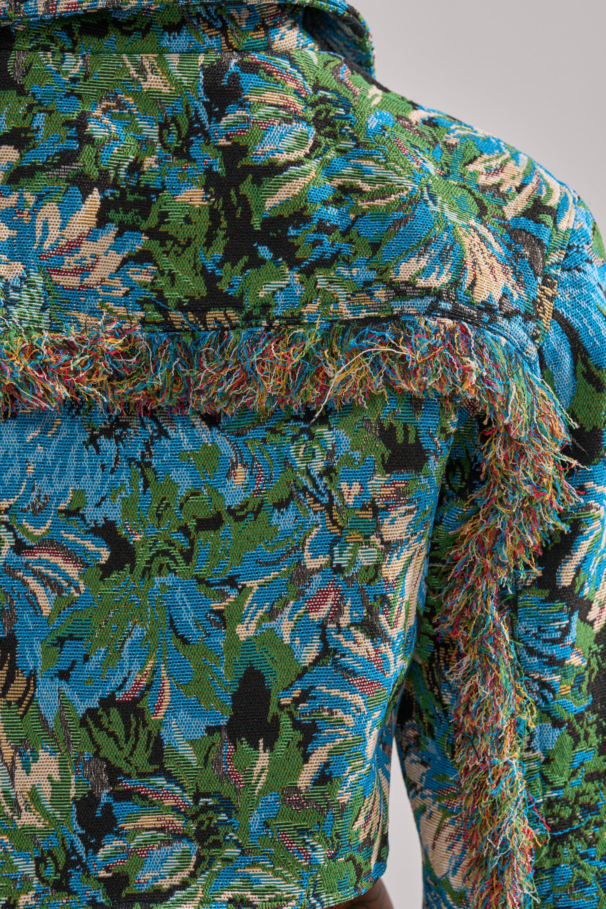 Close-up of the TRY ME TAPESTRY BOMBER, a vibrant cropped jacket featuring multicolored floral jacquard in green, blue, and black with textured fringed details for a dimensional, tactile effect. 9