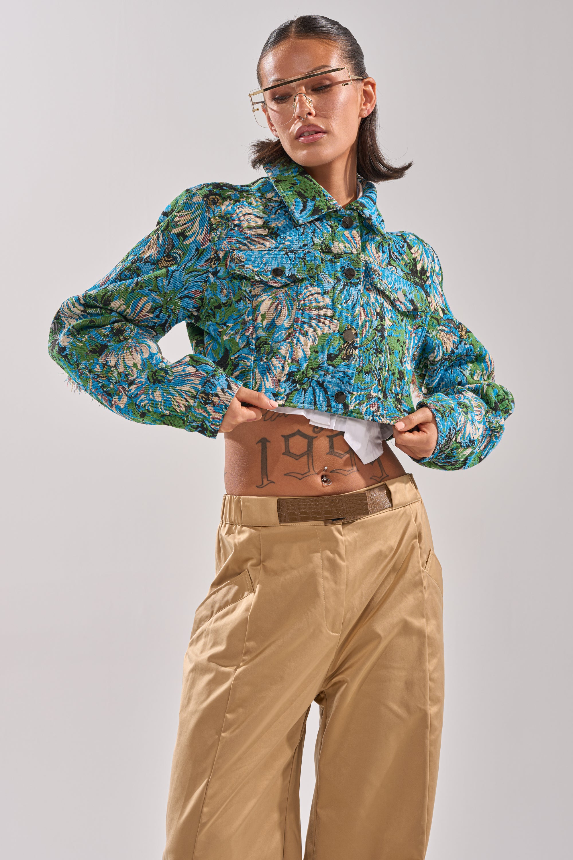 A person poses confidently in the TRY ME TAPESTRY BOMBER, tan pants, and transparent glasses. Their hair is tied back, and a "199" stomach tattoo is visible. 3