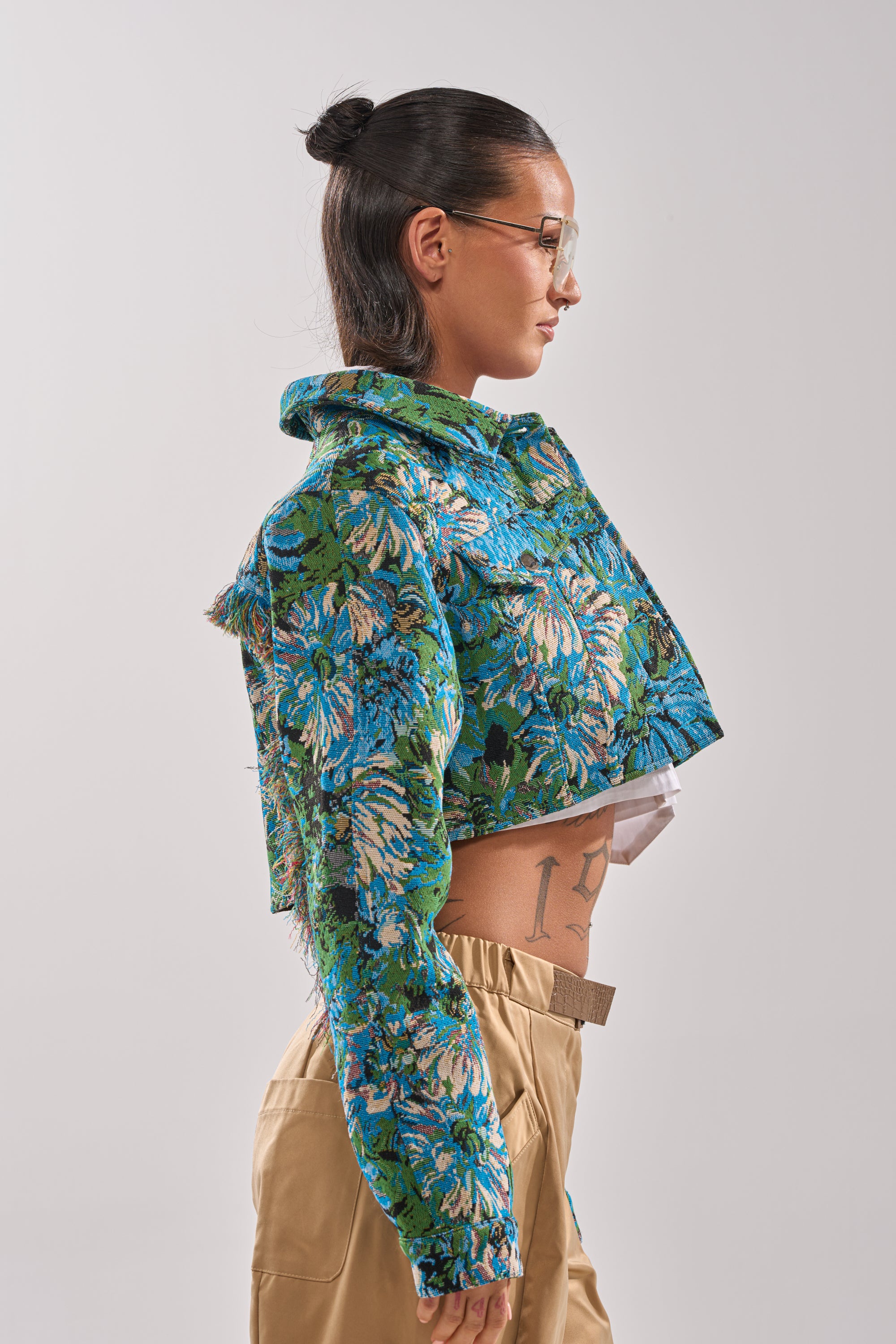 A woman with dark hair in a bun wears sunglasses and the TRY ME TAPESTRY BOMBER, styled with beige pants. She stands in profile against a plain background, revealing a tattoo on her side. 4
