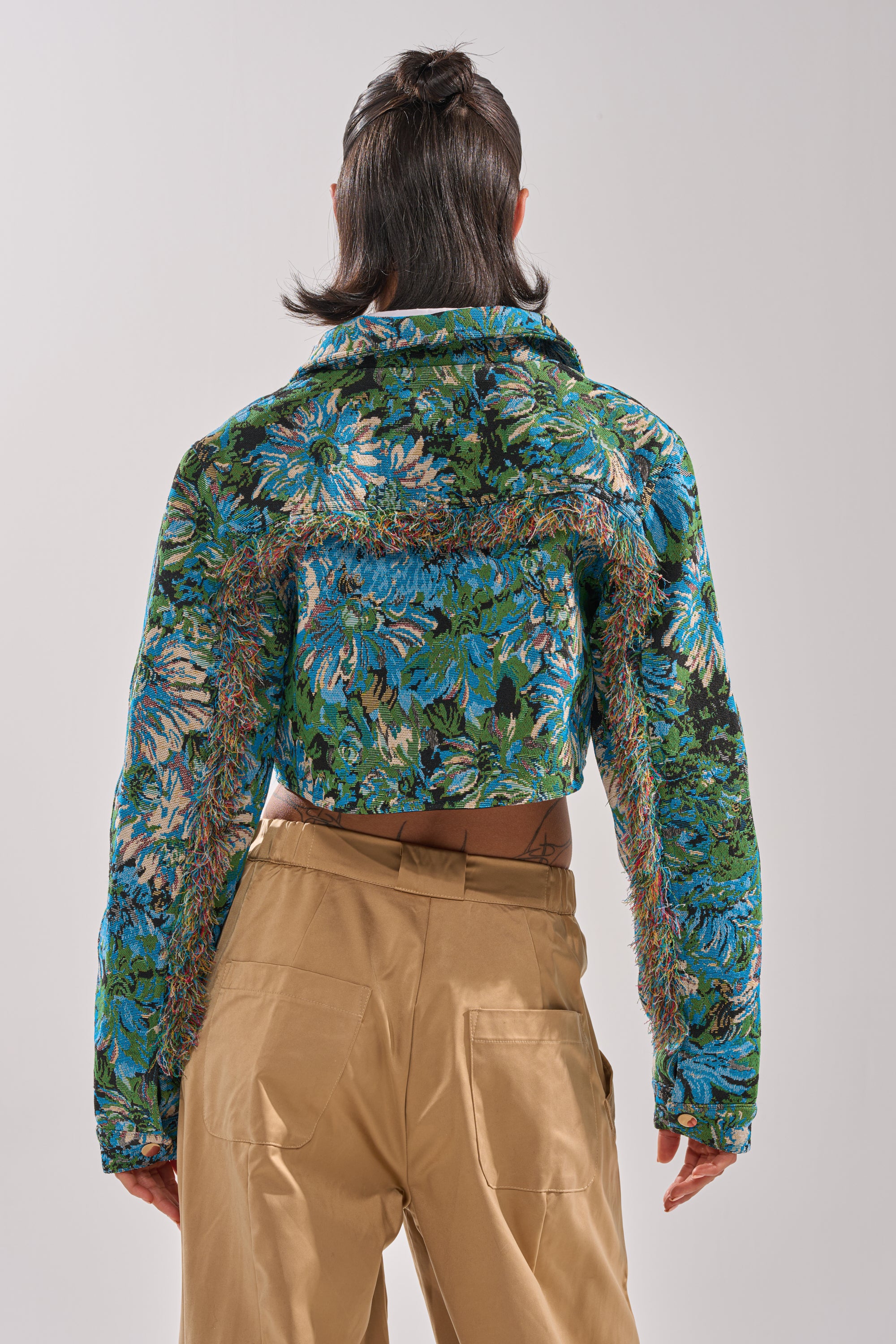 A person faces away from the camera, wearing high-waisted light brown pants and the TRY ME TAPESTRY BOMBER—a blue and green floral jacquard jacket—against a plain background. 5