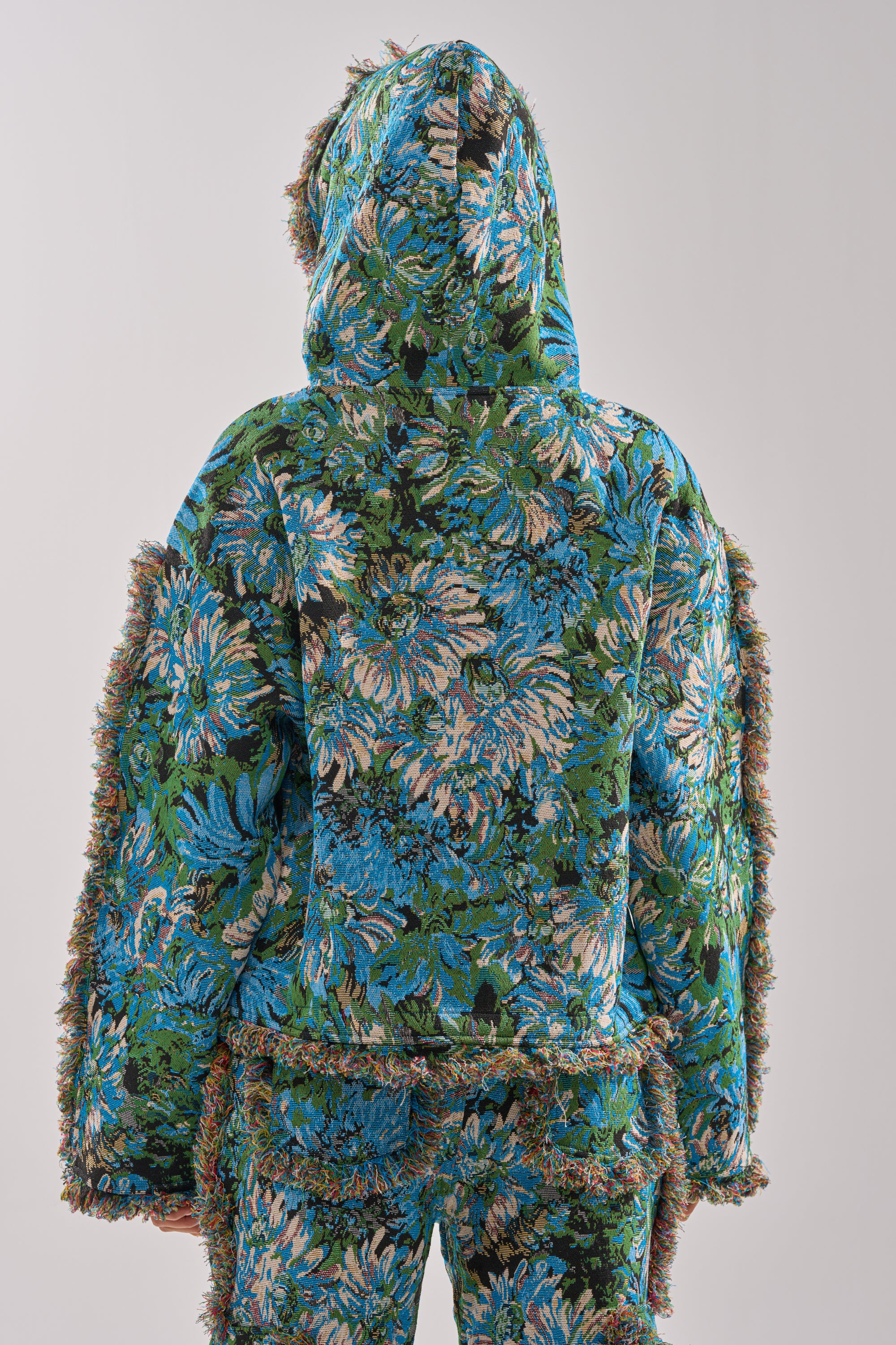 Person stands with their back to the camera, wearing the TRY ME TAPESTRY SWEATSHIRT and matching pants featuring a blue and green floral tapestry pattern with textured edges, set against a plain light background.