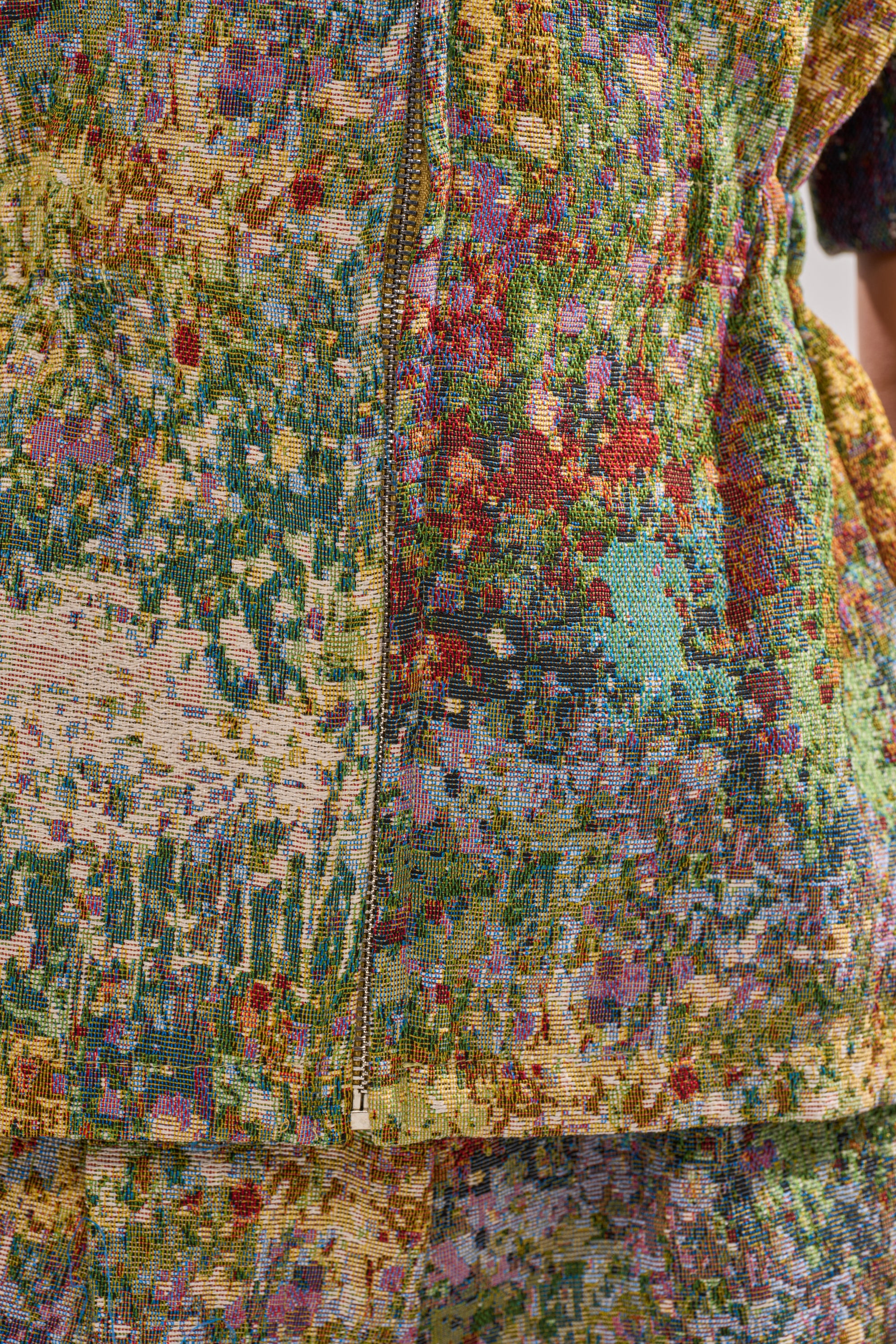 Close-up of the DEEP IN THE SEA BROCADE BLOUSE, featuring a textured jacquard fabric with an abstract, multicolored pattern in green, yellow, red, and blue. A visible zipper runs vertically through the center of this striking top.